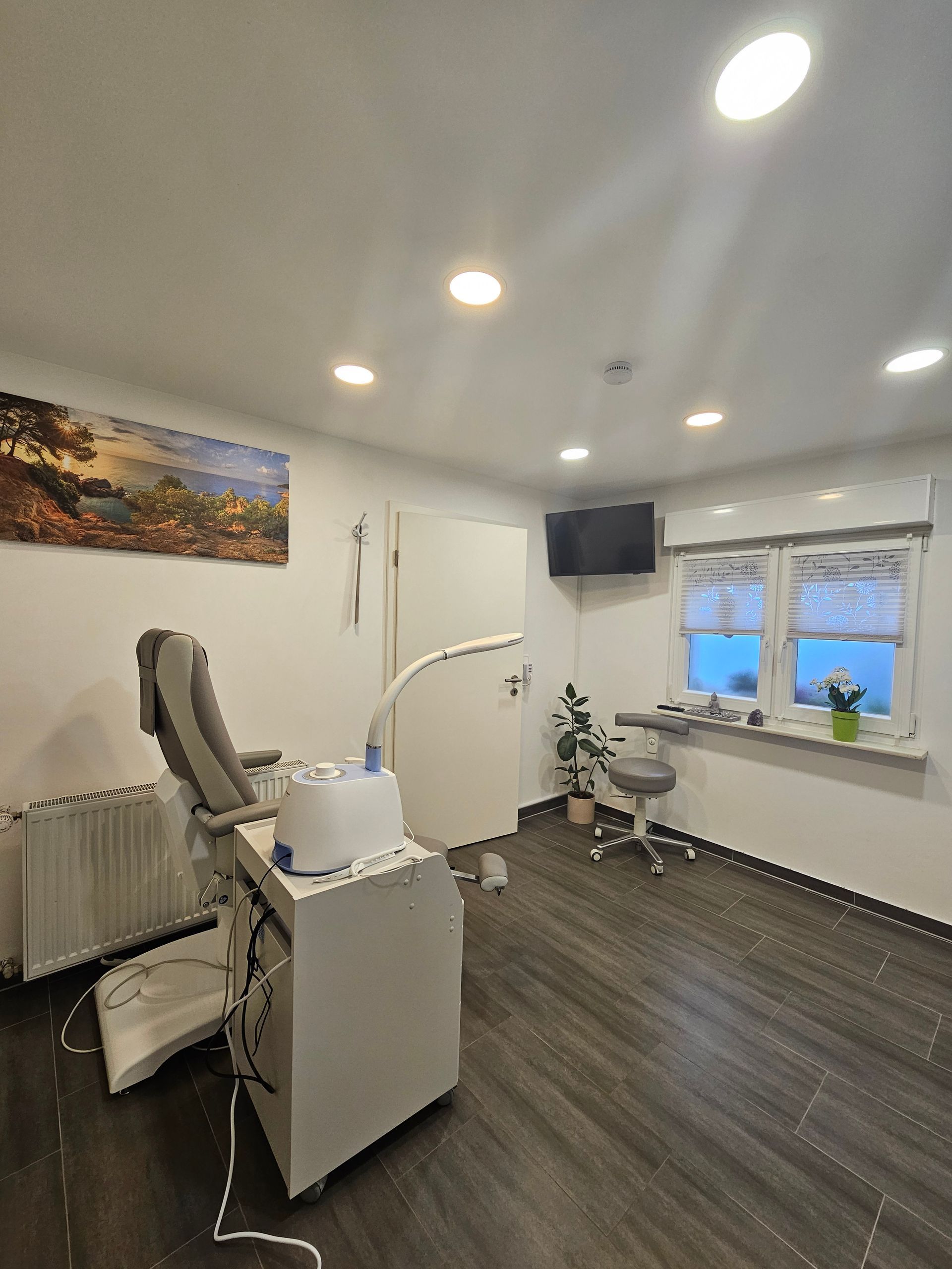 Moderner Zahnarztbehandlungsraum mit Stuhl, Geräten, Wandbildern, Fernseher und Fenster.