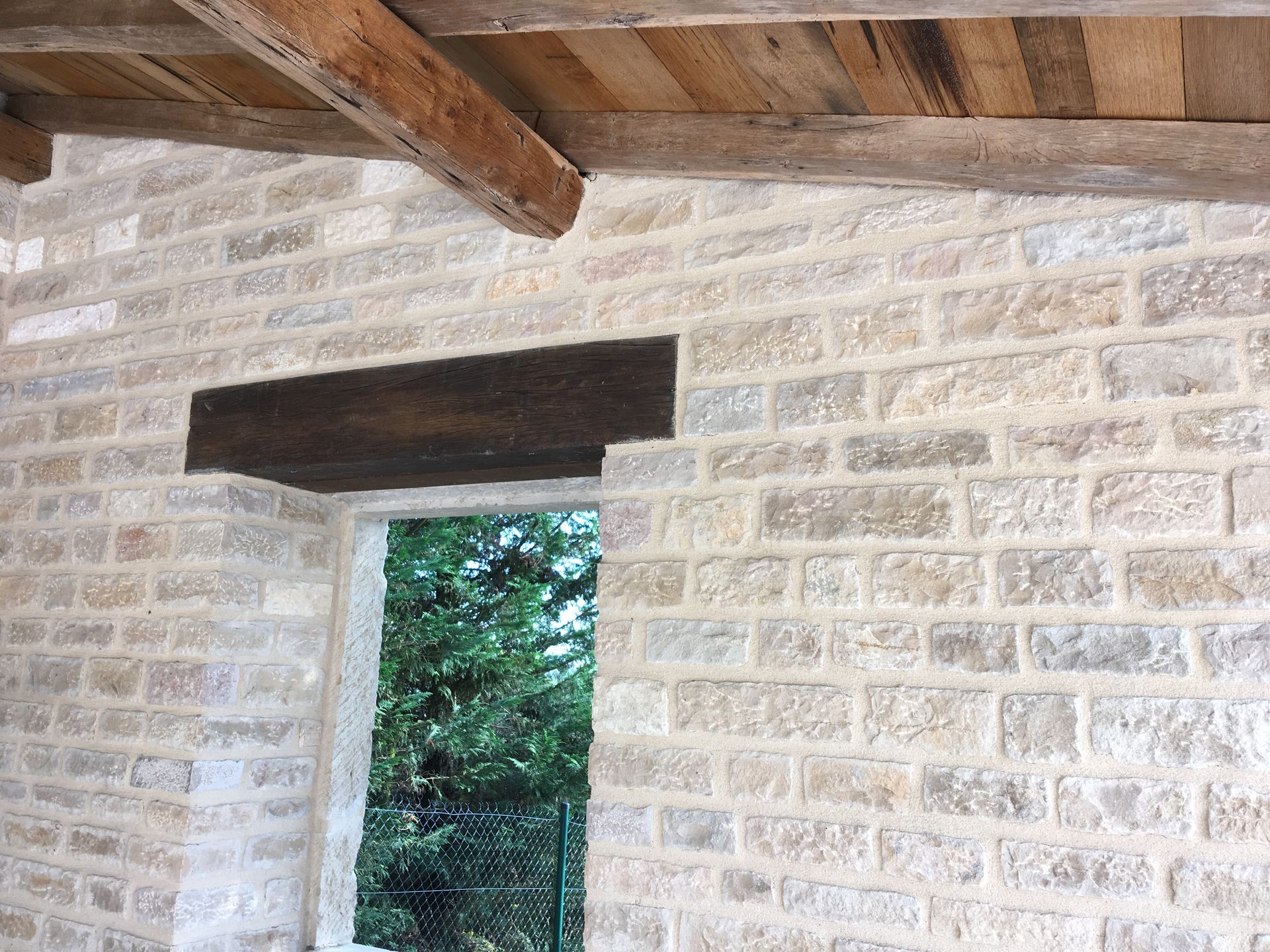 Mur en pierre avec des détails de construction et une fenêtre. La structure semble ancienne et bien entretenue.