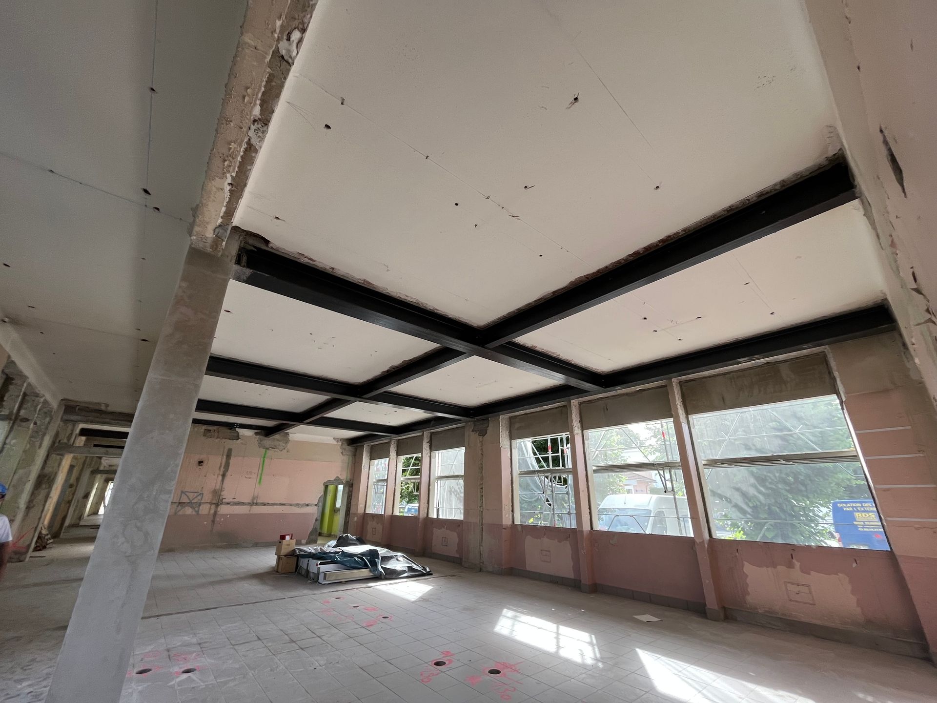 Intérieur d'un bâtiment en cours de rénovation avec des structures en métal et des murs en béton. Des fenêtres laissent entrer la lumière naturelle.