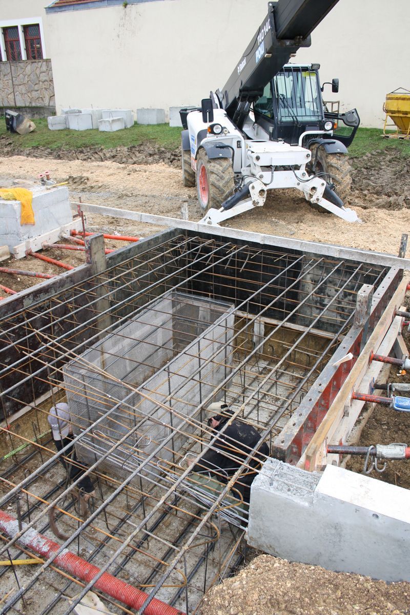 Structure en béton avec des armatures en acier visibles, en cours de construction. Des échafaudages et des barres de renforcement sont visibles.