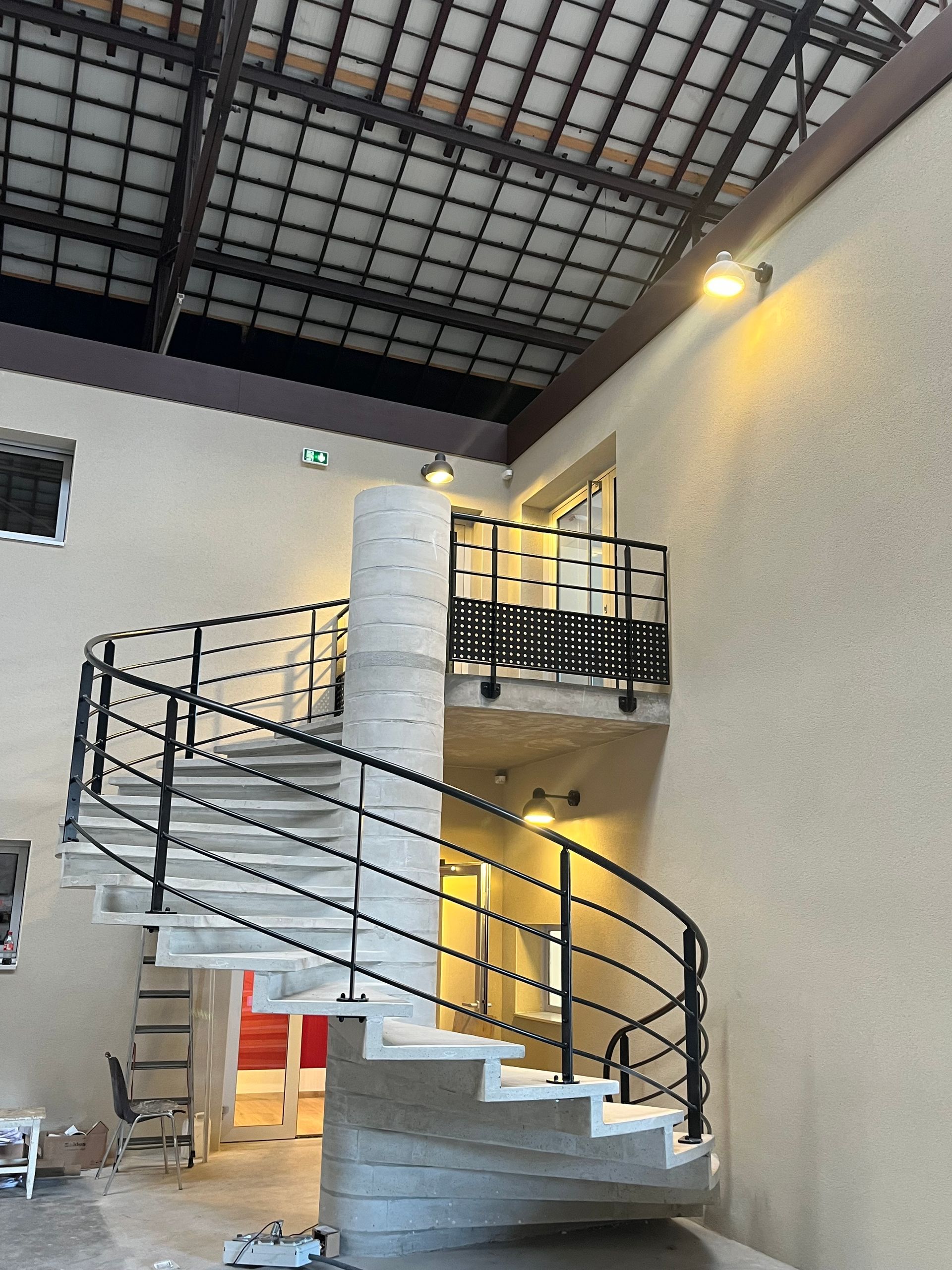 Escalier moderne en métal avec des rampes et des structures en verre. L'escalier est situé dans un bâtiment avec des murs blancs et un éclairage moderne.