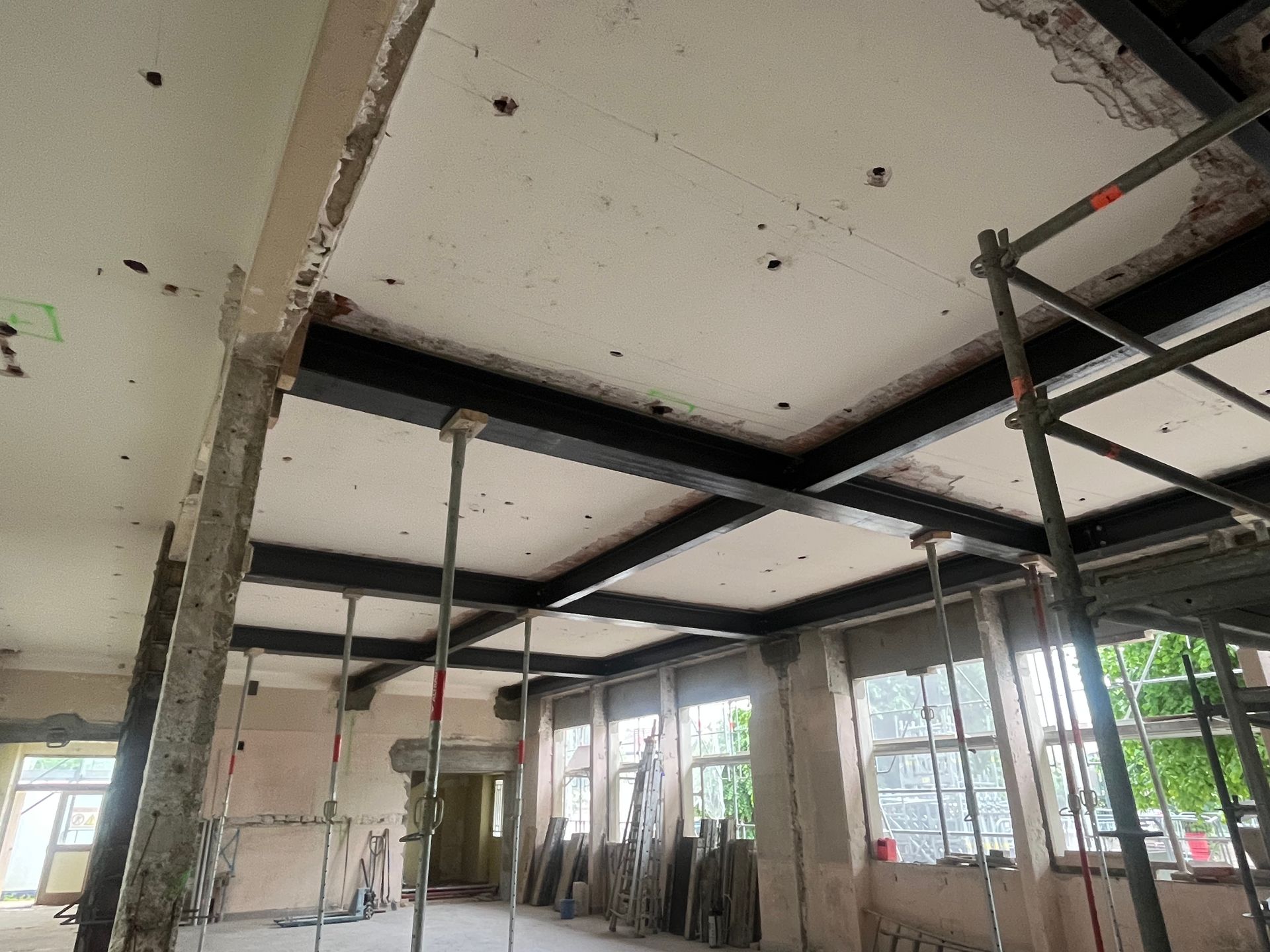  Intérieur d'un bâtiment en cours de rénovation avec des structures en métal et des murs en béton. Des fenêtres laissent entrer la lumière naturelle.