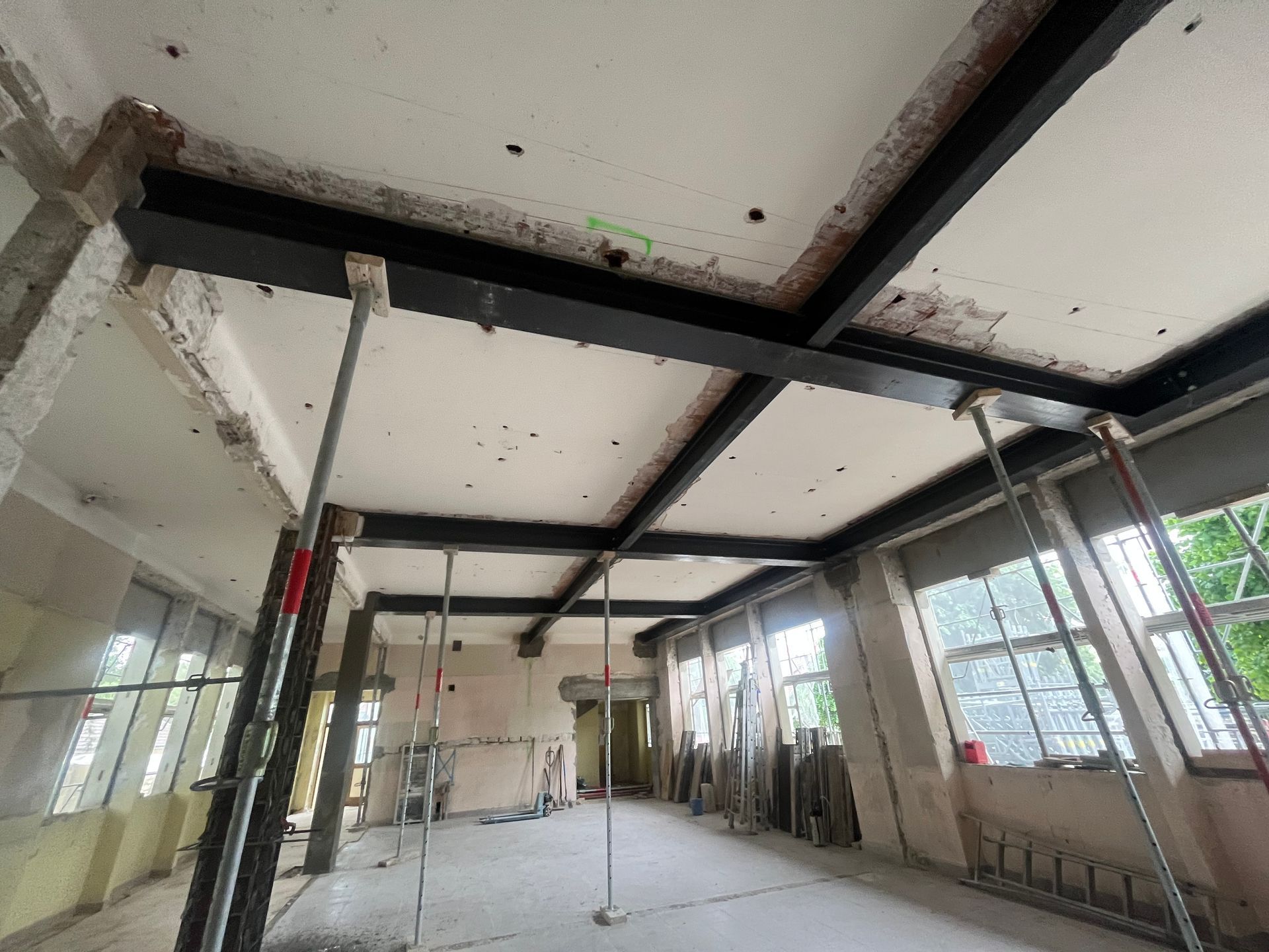  Intérieur d'un bâtiment en cours de rénovation avec des poutres IPN en métal et des murs en béton. Des fenêtres laissent entrer la lumière naturelle.