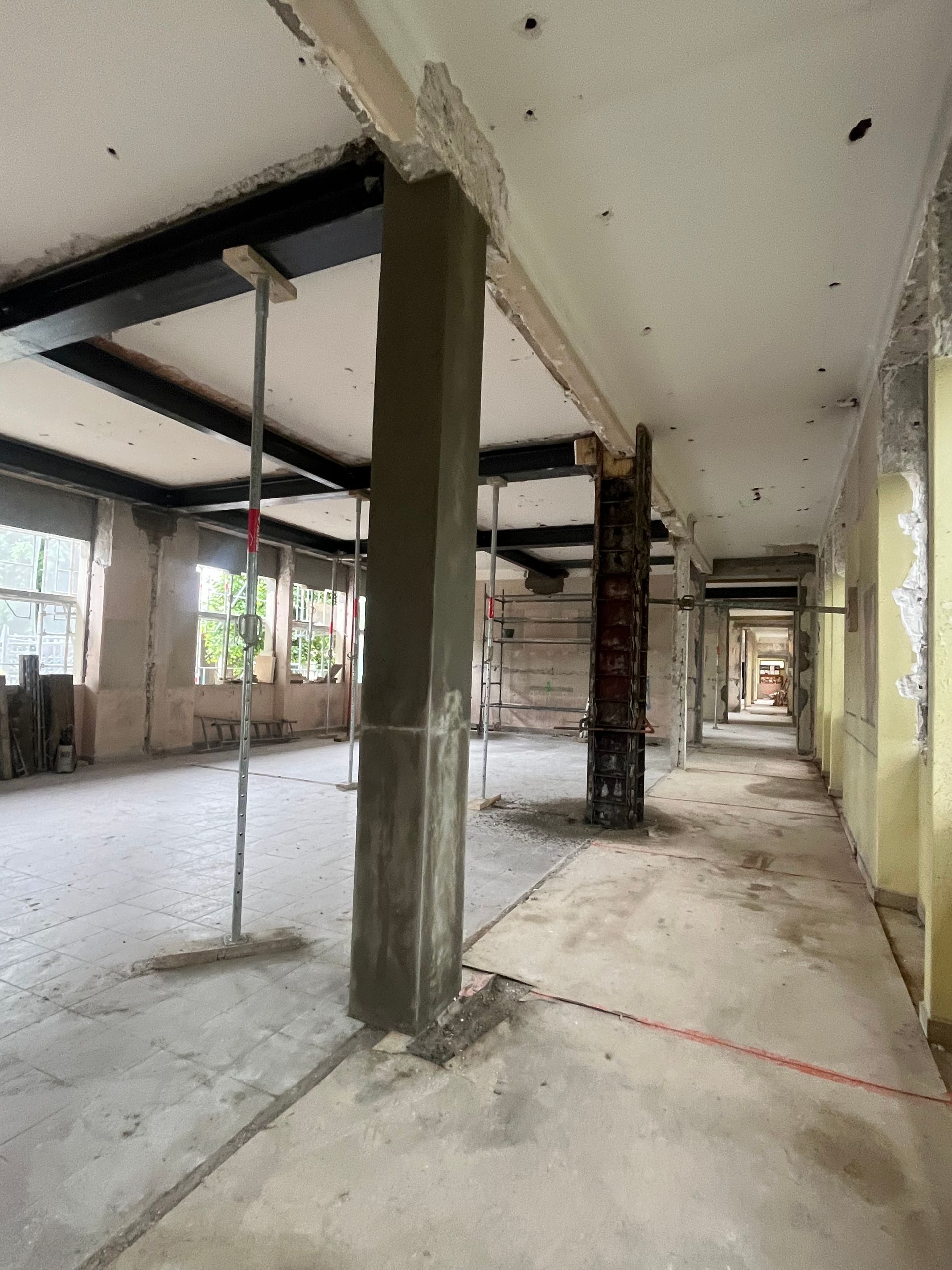 Intérieur d'un bâtiment en cours de rénovation avec des structures en métal et des murs en béton. Des outils et des matériaux de construction sont éparpillés sur le sol.