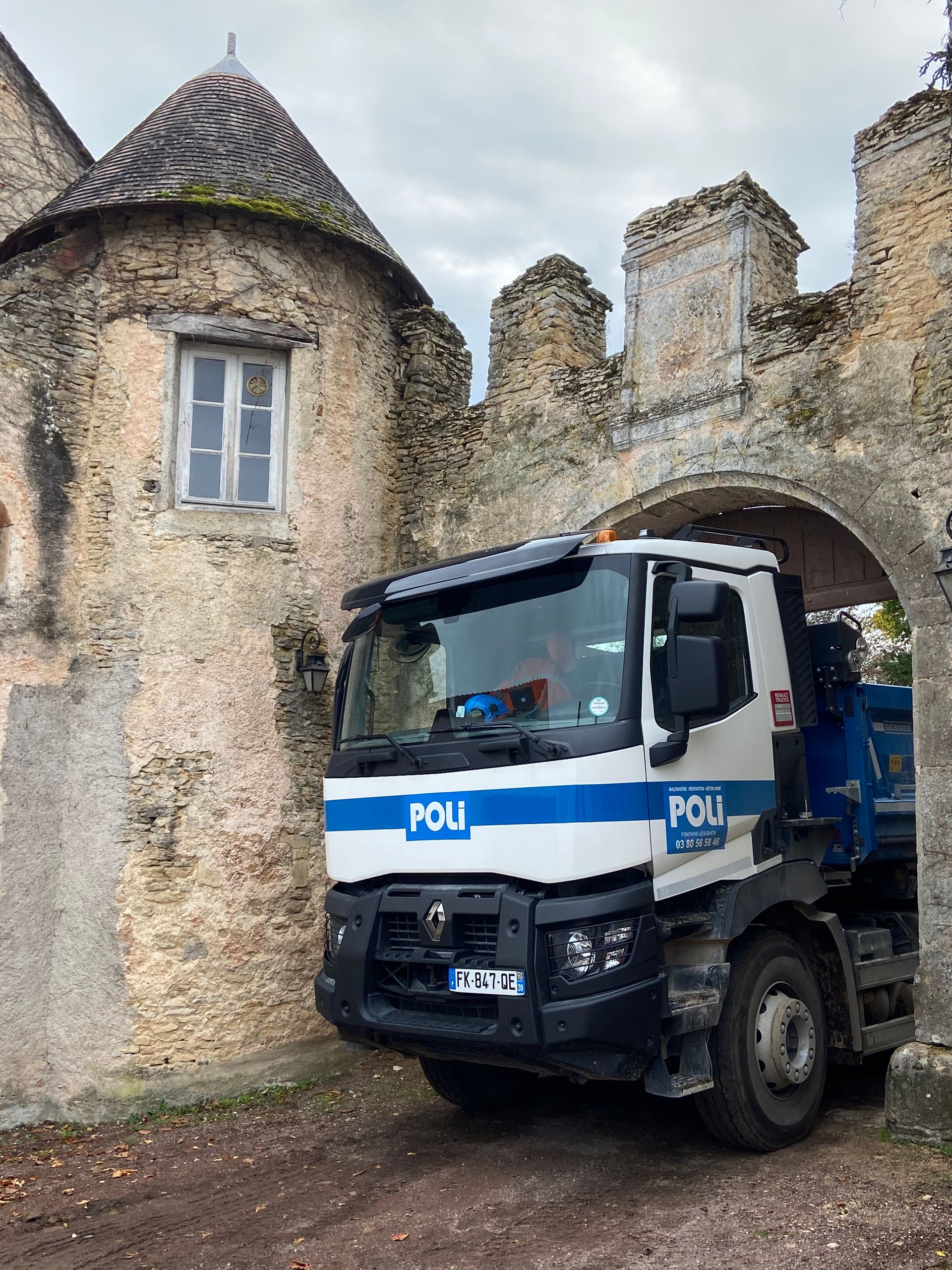 Camion de chantier garé devant un bâtiment ancien sous une arche.
