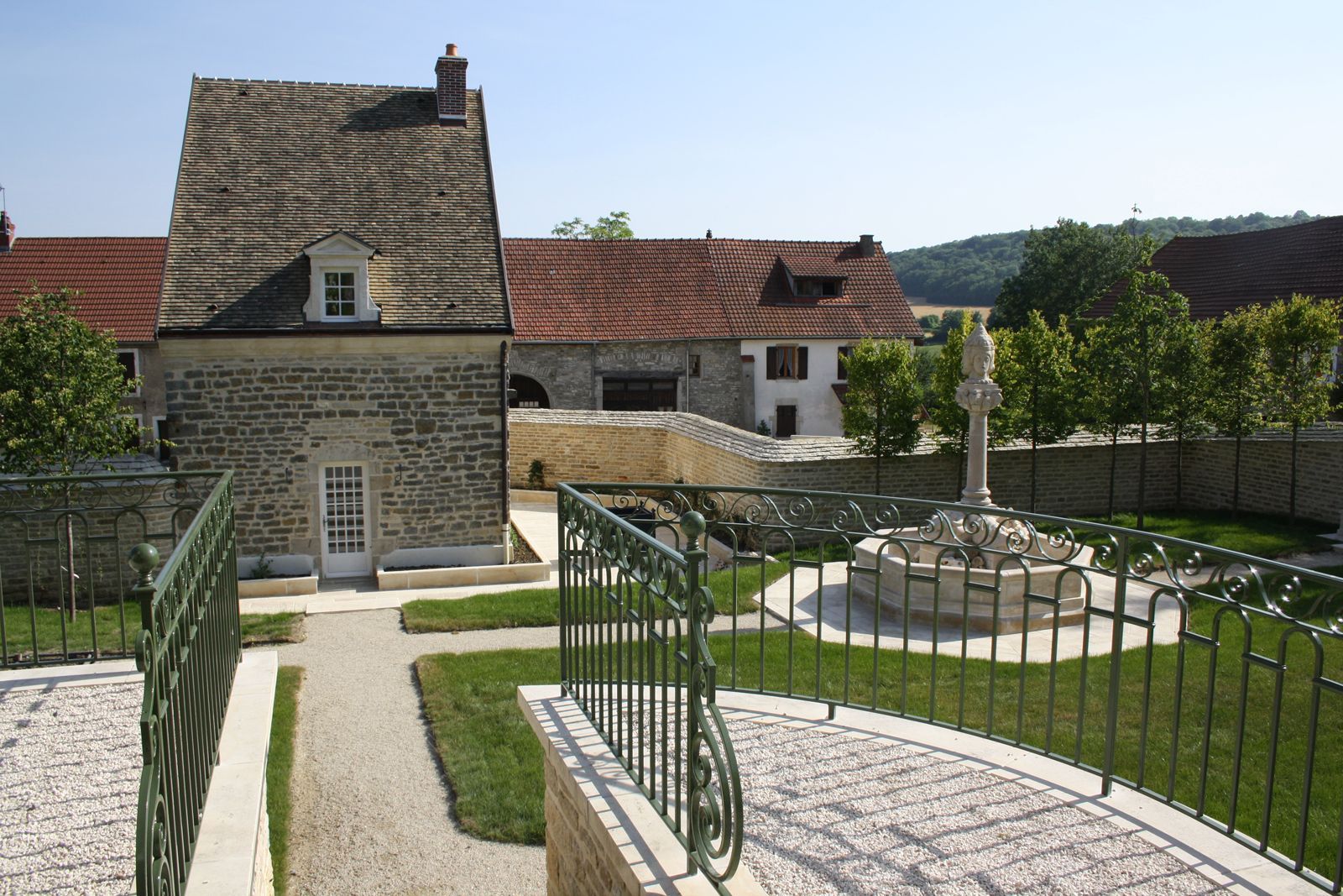 Maison ancienne avec un jardin bien entretenu et une statue au centre.