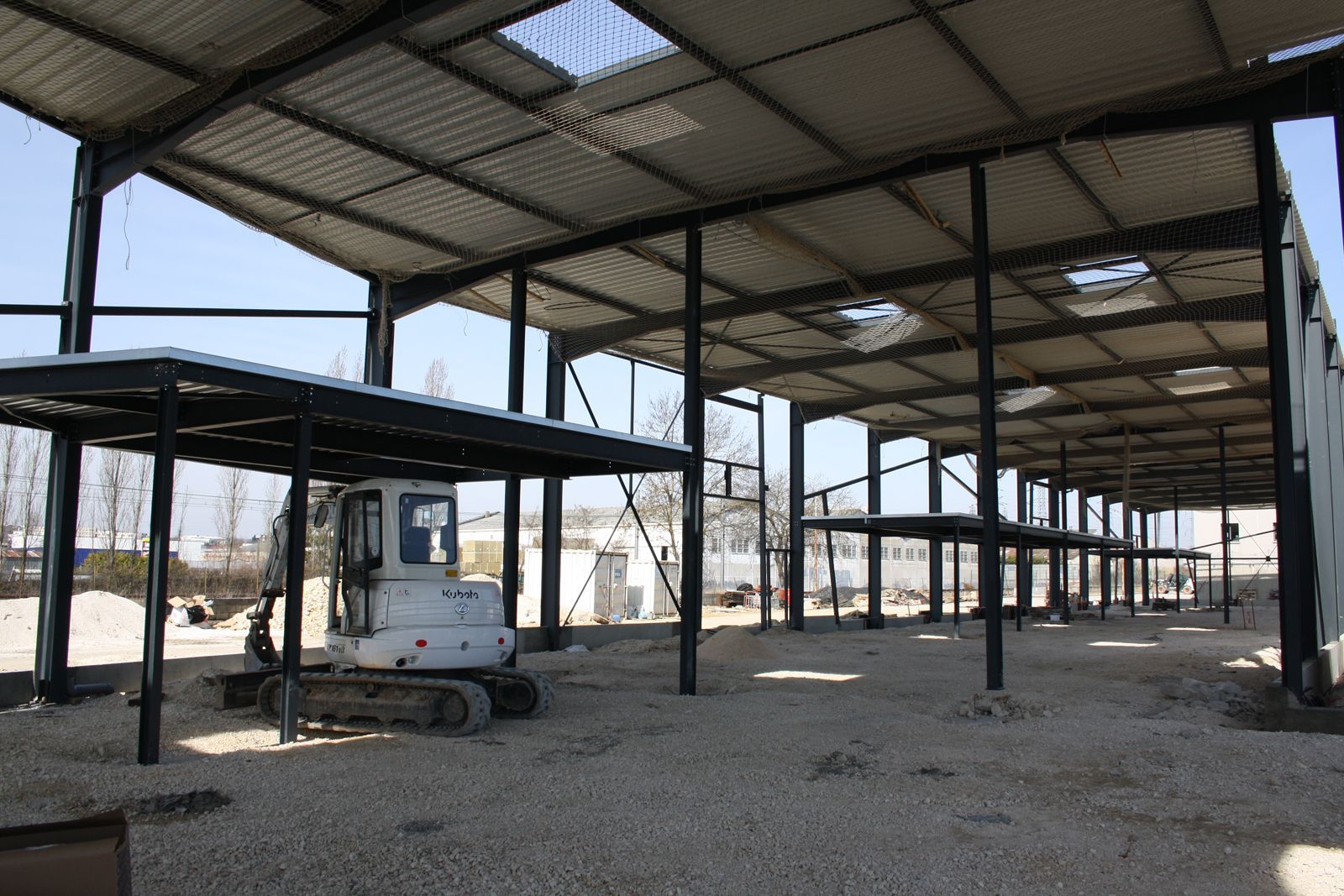 Intérieur d'un bâtiment industriel en construction avec des structures en métal et des murs en béton. Des échafaudages sont visibles pour soutenir la structure.
