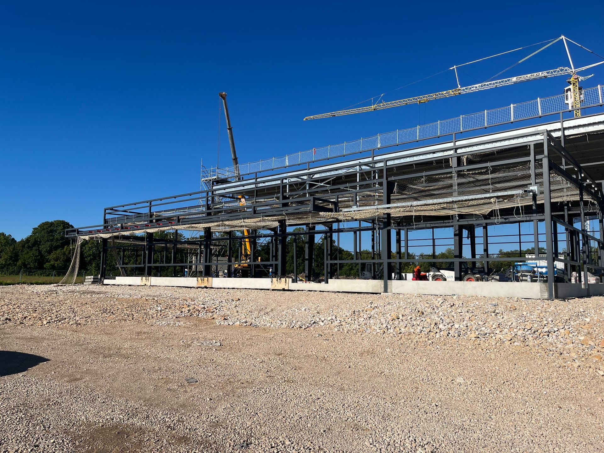 Bâtiment industriel en construction avec des structures en métal. Des grues et des échafaudages sont visibles.