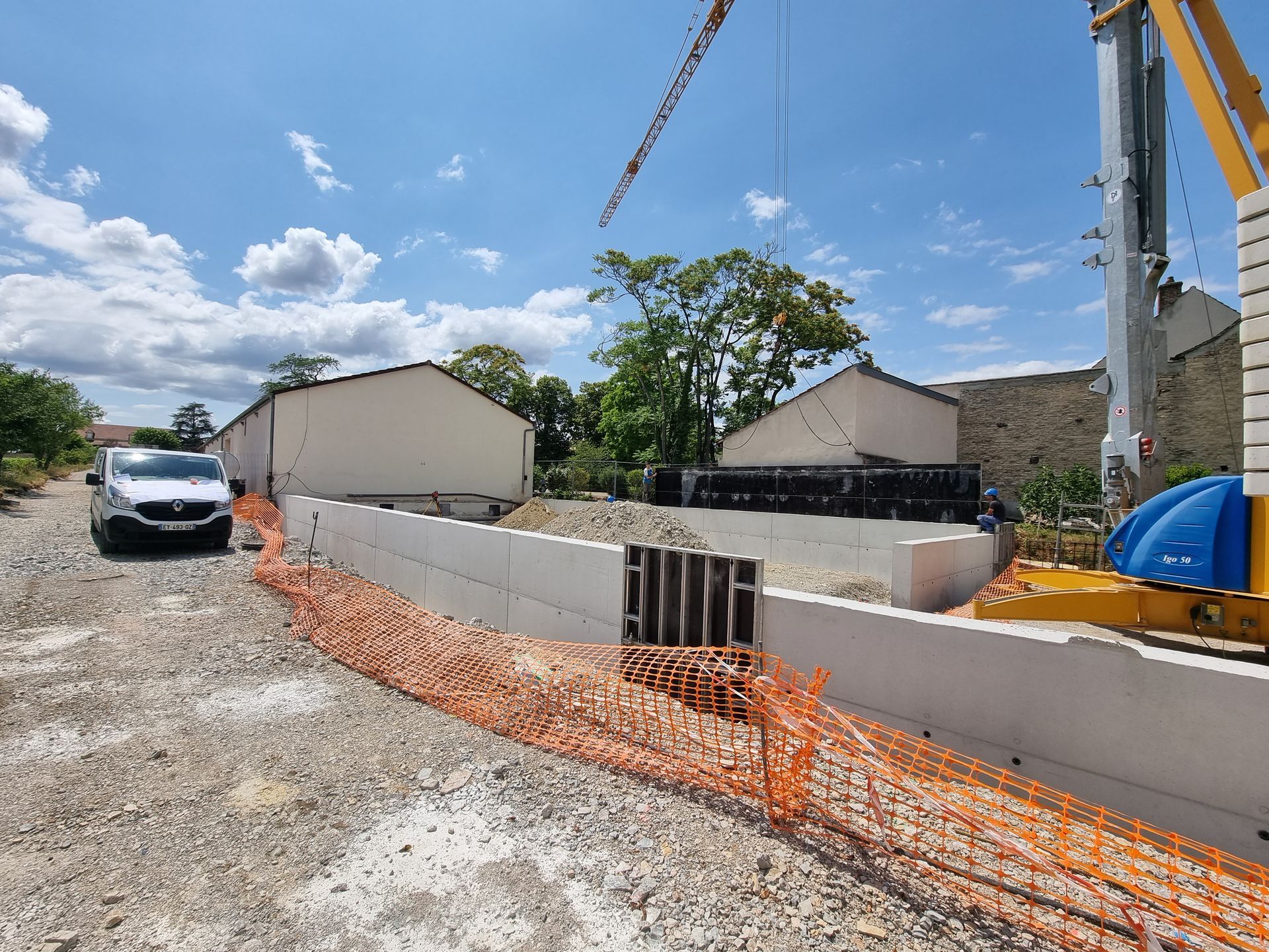 Chantier de construction avec des matériaux de construction et des structures en béton. Des bâtiments en arrière-plan sont partiellement construits.
