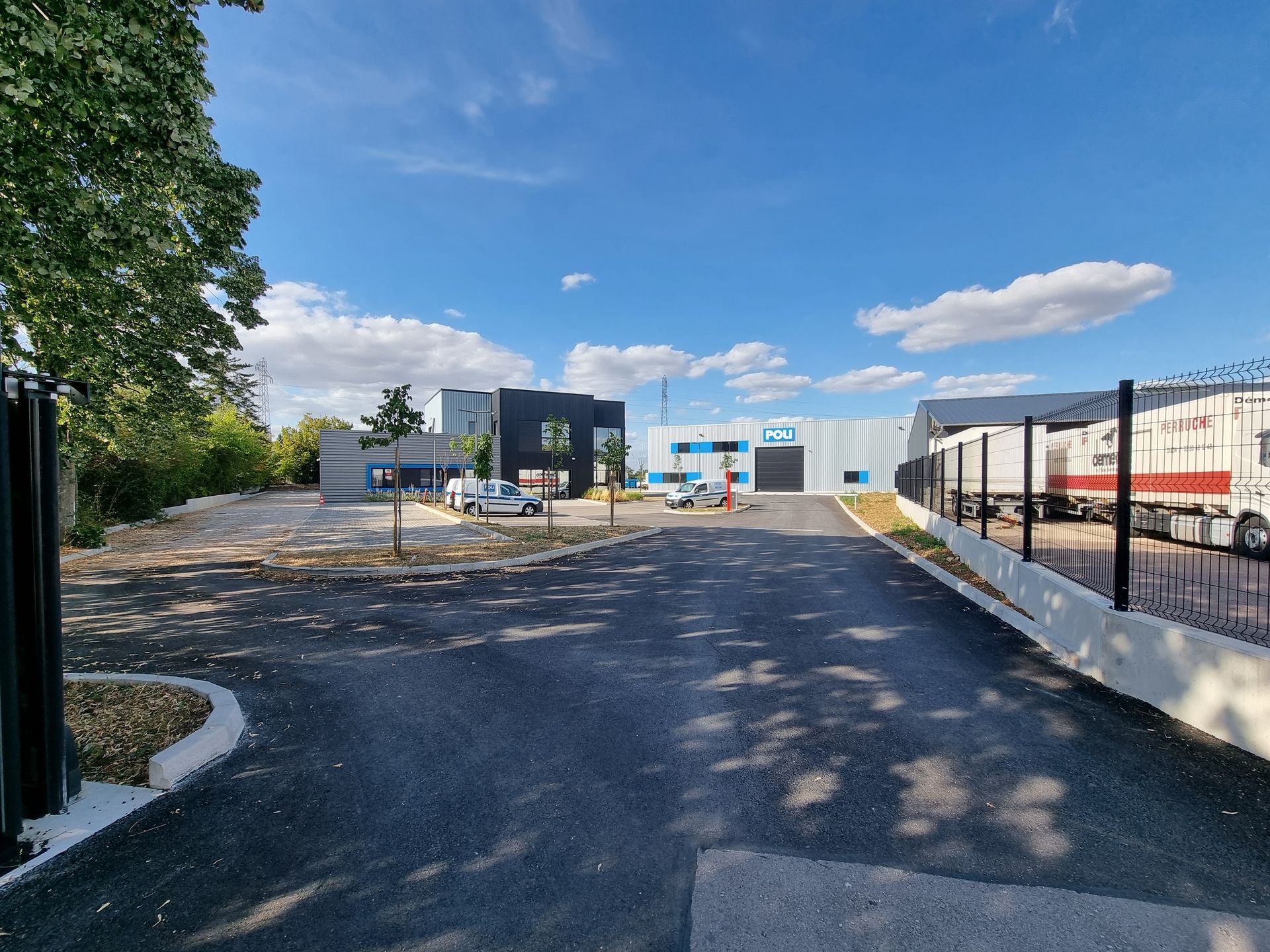 Route menant à un bâtiment industriel avec des arbres et des clôtures.