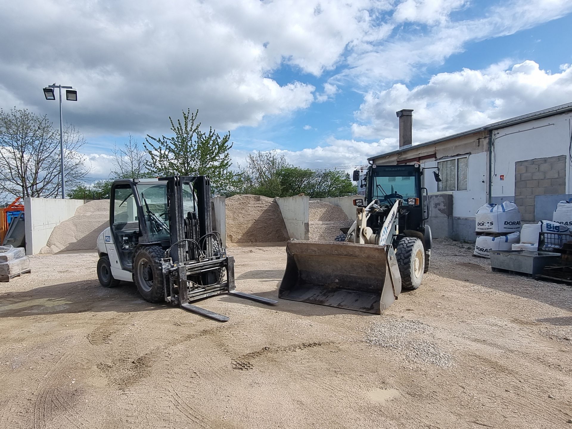 Un chariot élévateur et un tracteur avec godet côte à côte.