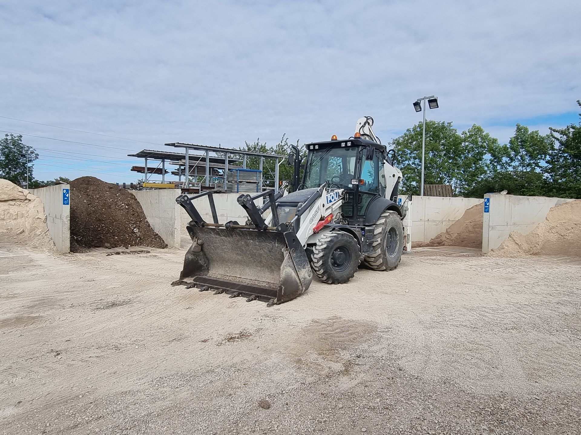 Tractopelle avec godet devant une réserve de matériaux.