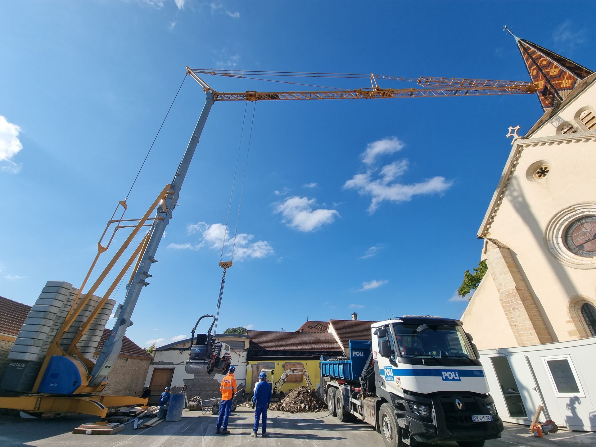 Grue de construction sur en train d'intervenir sur le clocher d'une église de couleur beige.
