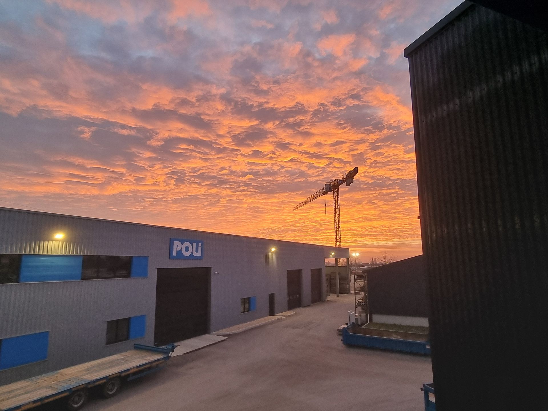 Bâtiment industriel avec une grue en arrière-plan sous un ciel au coucher du soleil.