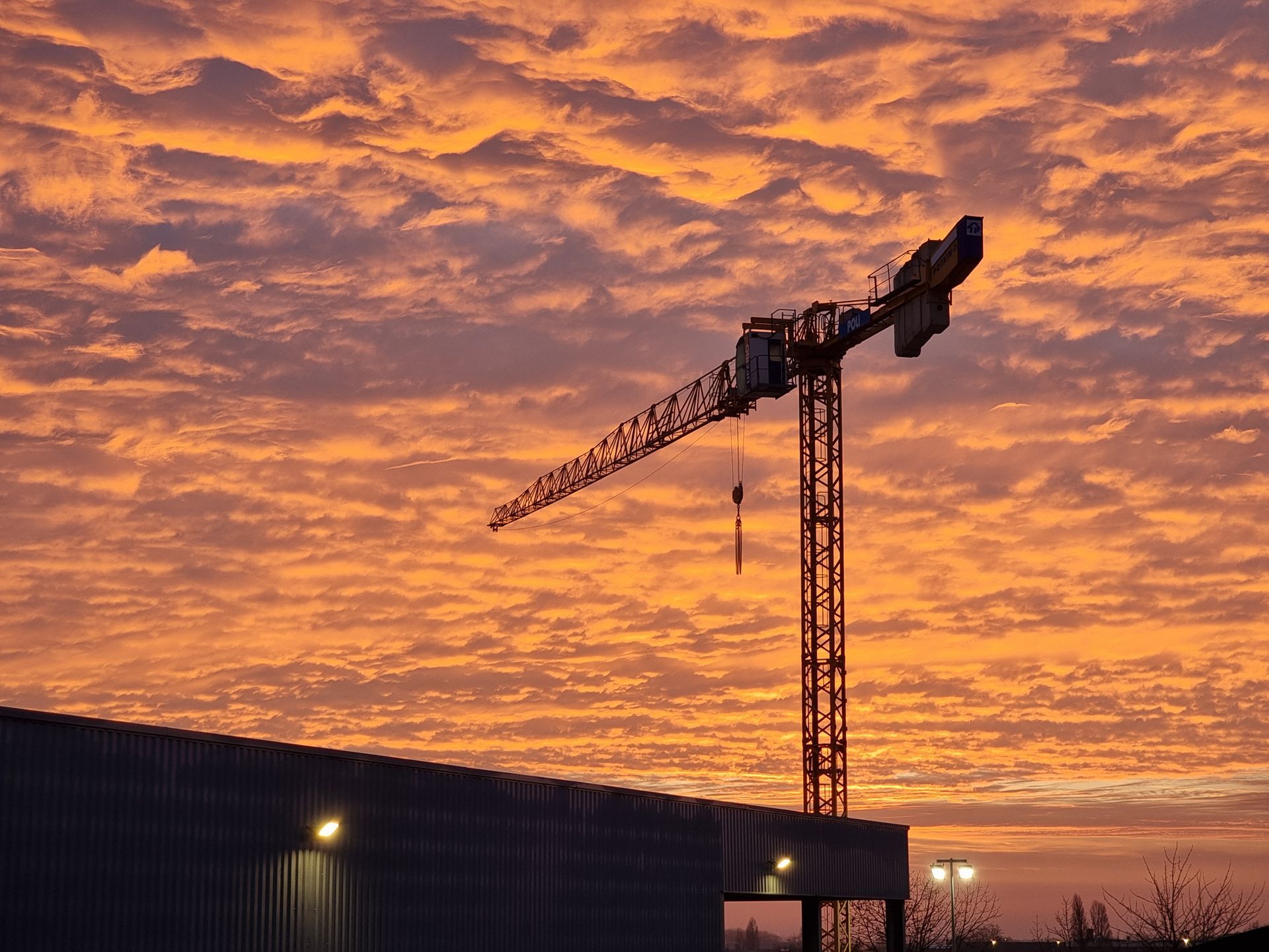 Grue de construction silhouettée contre un ciel coloré au coucher du soleil.