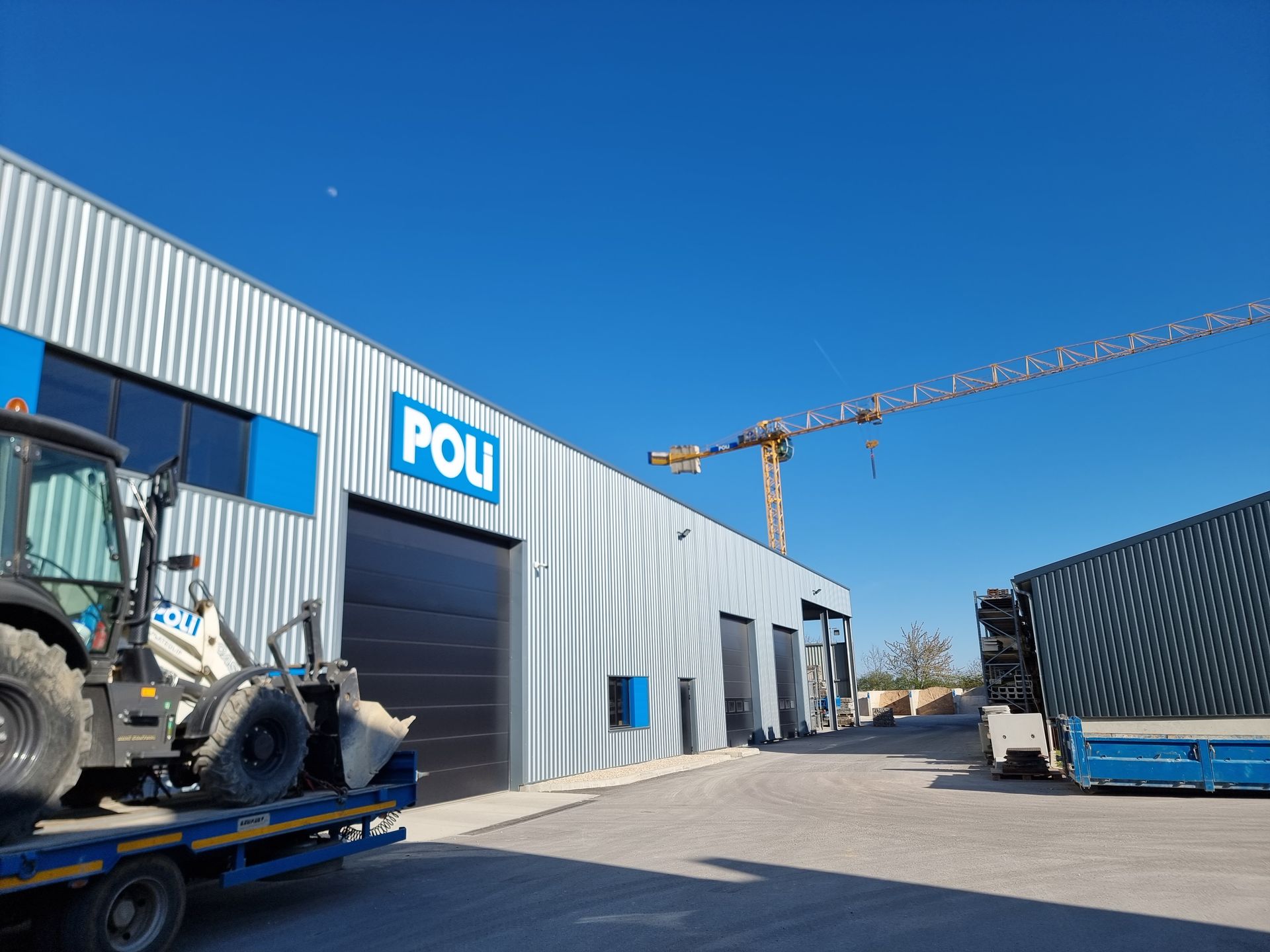 Grue de construction devant un bâtiment industriel sous un ciel bleu.