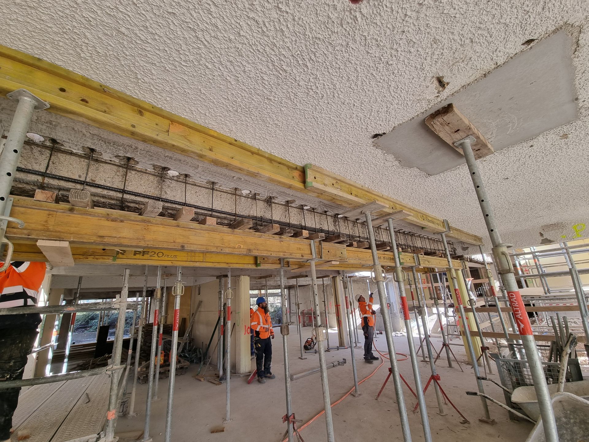 Intérieur d'un bâtiment en cours de rénovation avec des échafaudages et des structures en métal. Des ouvriers sont visibles en train de travailler sur le chantier.