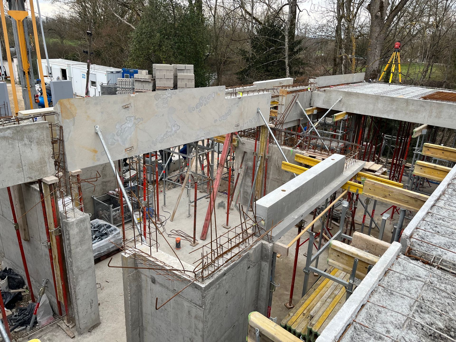 Structure en béton avec des armatures en acier visibles, en cours de construction. Des échafaudages et des barres de renforcement sont visibles.