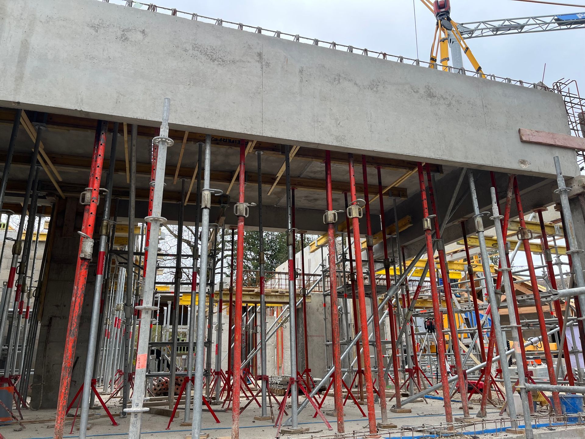 Structure en béton avec des armatures en acier visibles, en cours de construction. Des échafaudages et des barres de renforcement sont visibles.