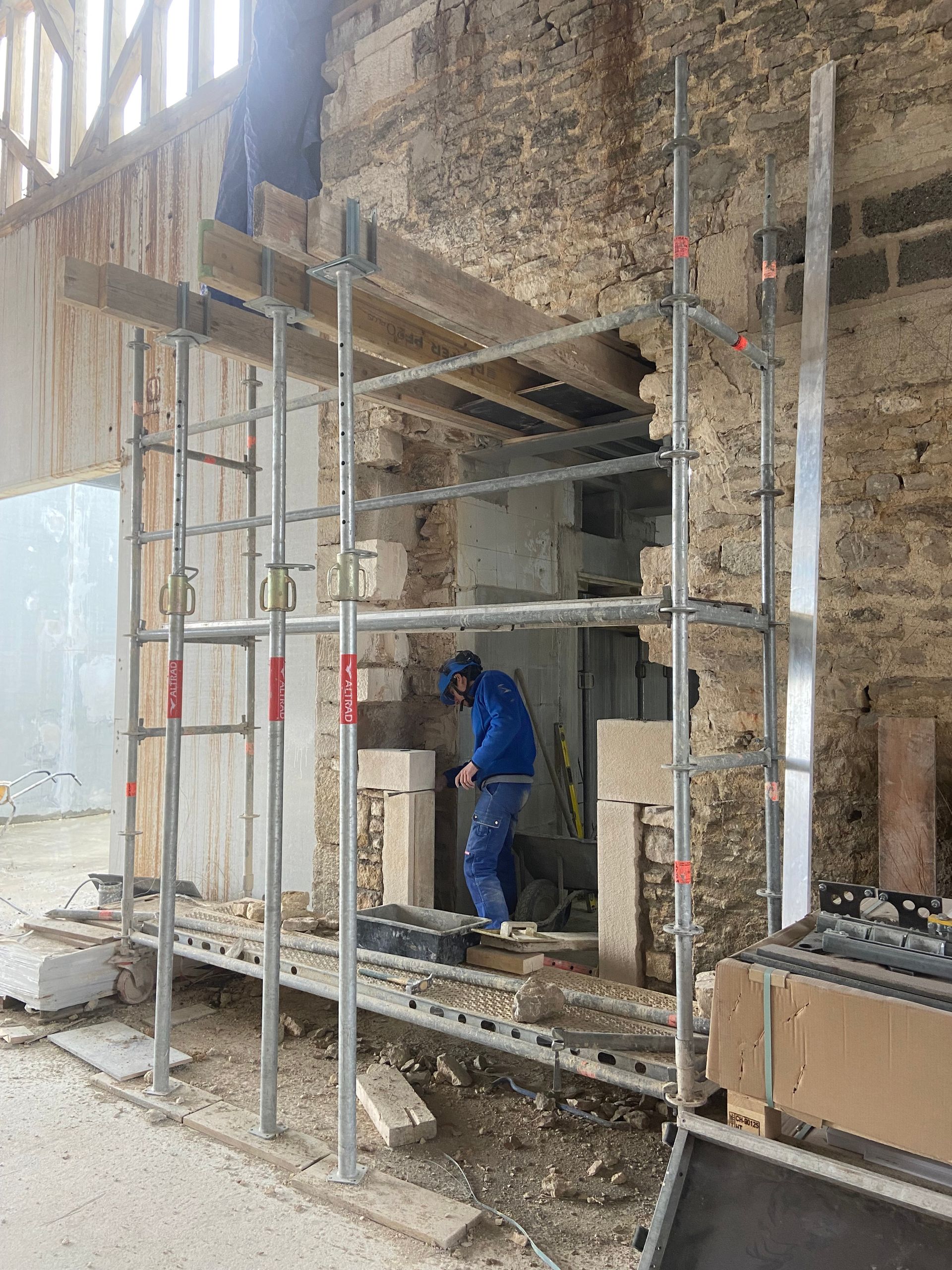 Travailleur sur un chantier de construction avec des structures en métal en train de refaire une ouverture dans un mur de pierre.