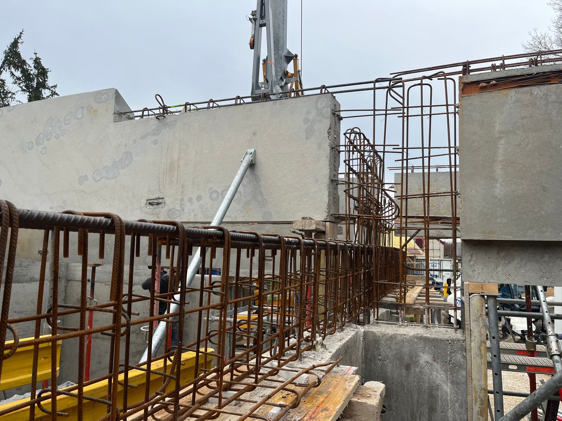 Structure en béton avec des armatures en acier visibles, en cours de construction. Des échafaudages et des barres de renforcement sont visibles.