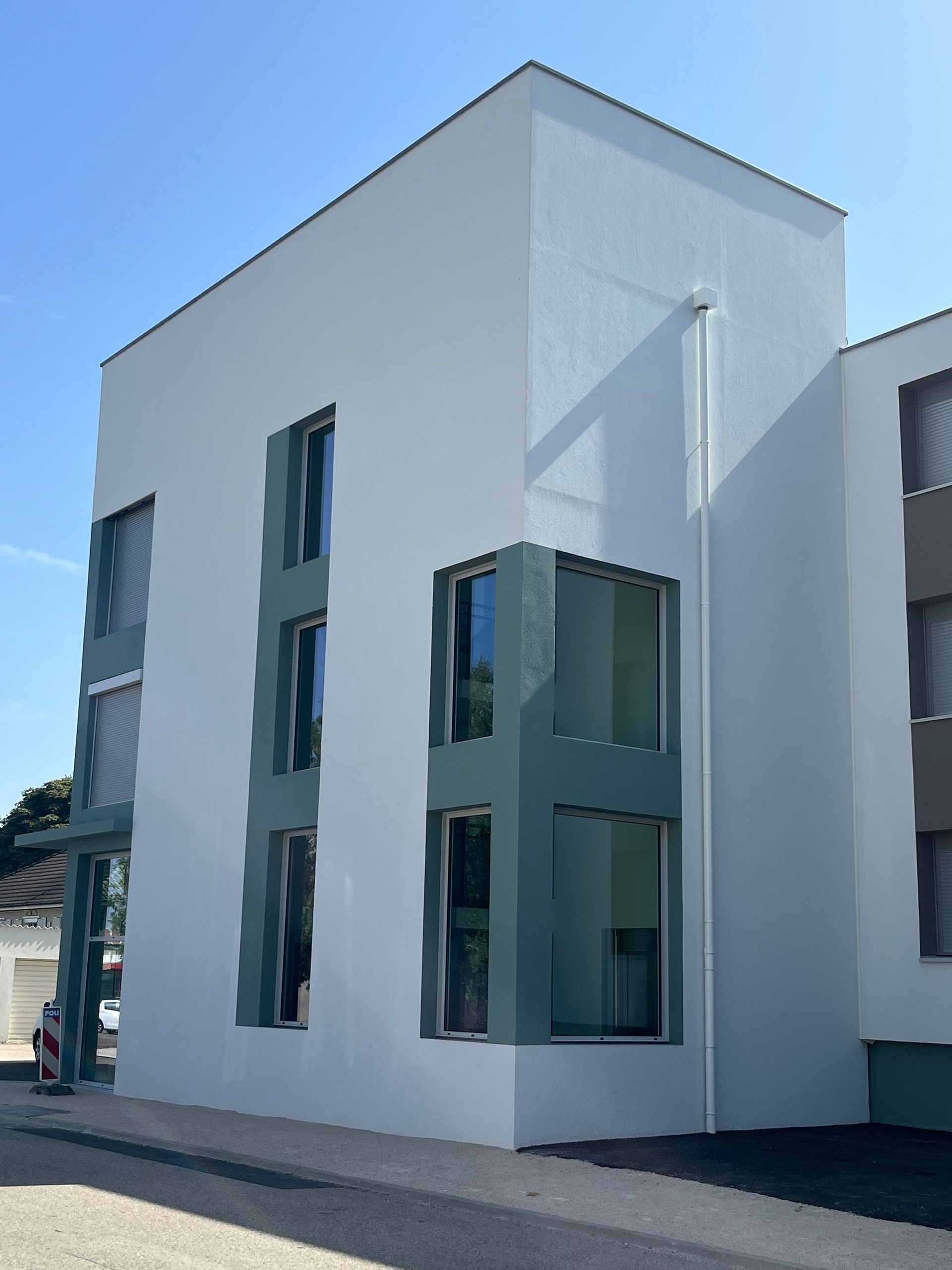 Bâtiment moderne avec une façade blanche et des fenêtres en métal vert.