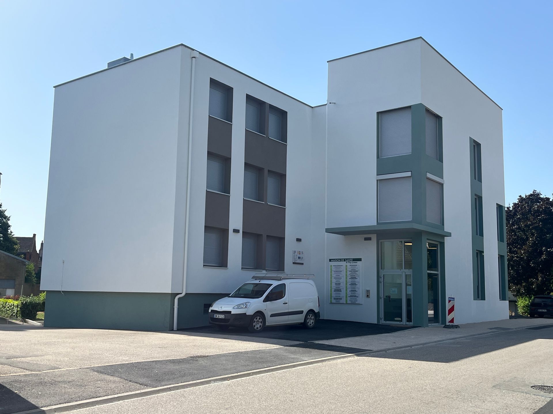 Bâtiment moderne avec une façade en bois et des structures en métal. Le bâtiment est entouré de verdure et le ciel est clair et ensoleillé.