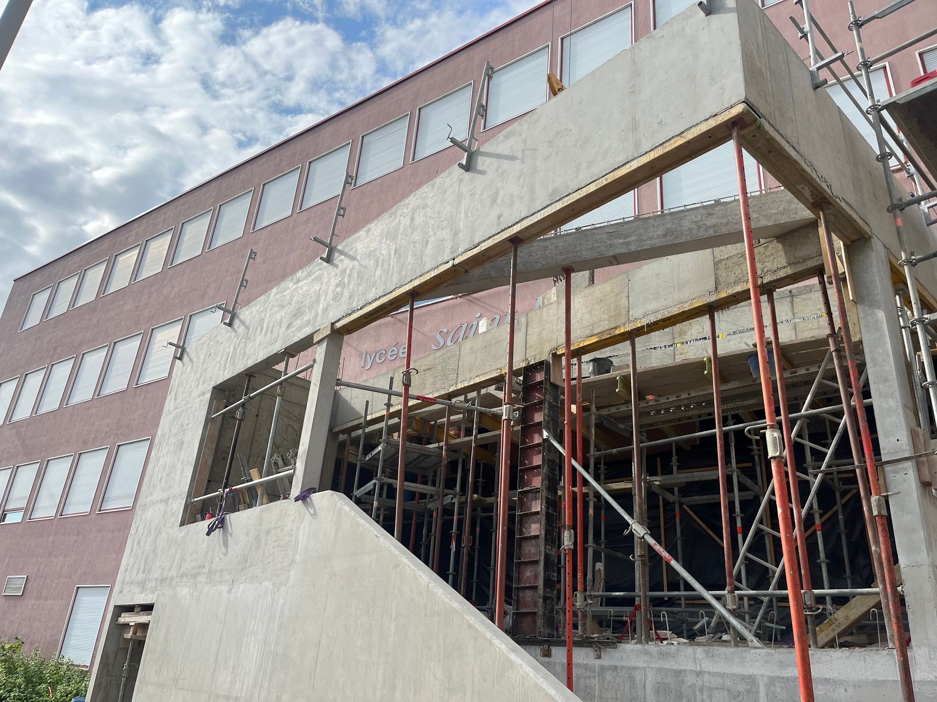Bâtiment en construction avec des échafaudages et des structures en béton. Des ouvriers sont visibles en train de travailler sur le chantier.