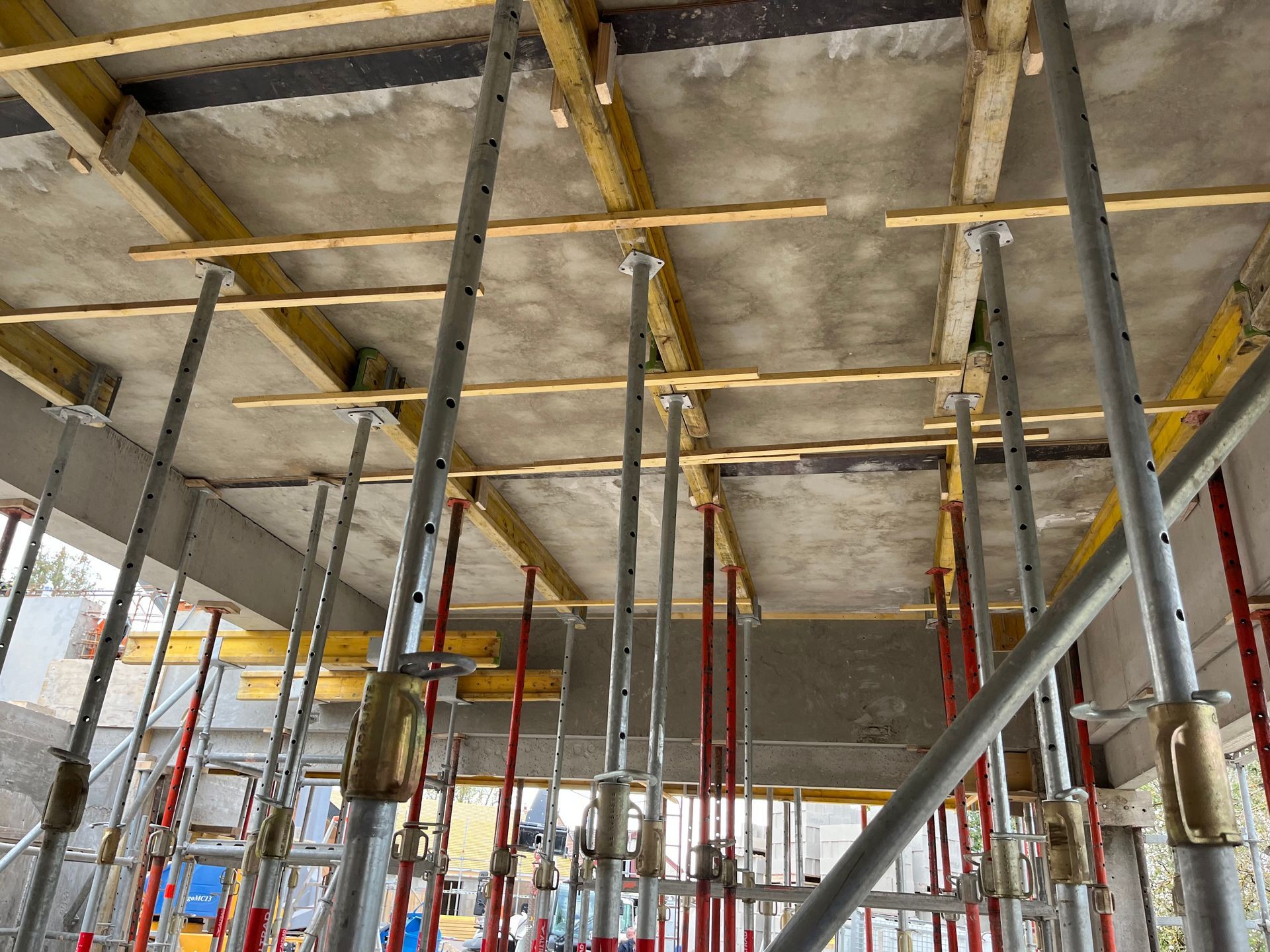 Structure en béton avec des armatures en acier visibles, en cours de construction. Des échafaudages et des barres de renforcement sont visibles.
