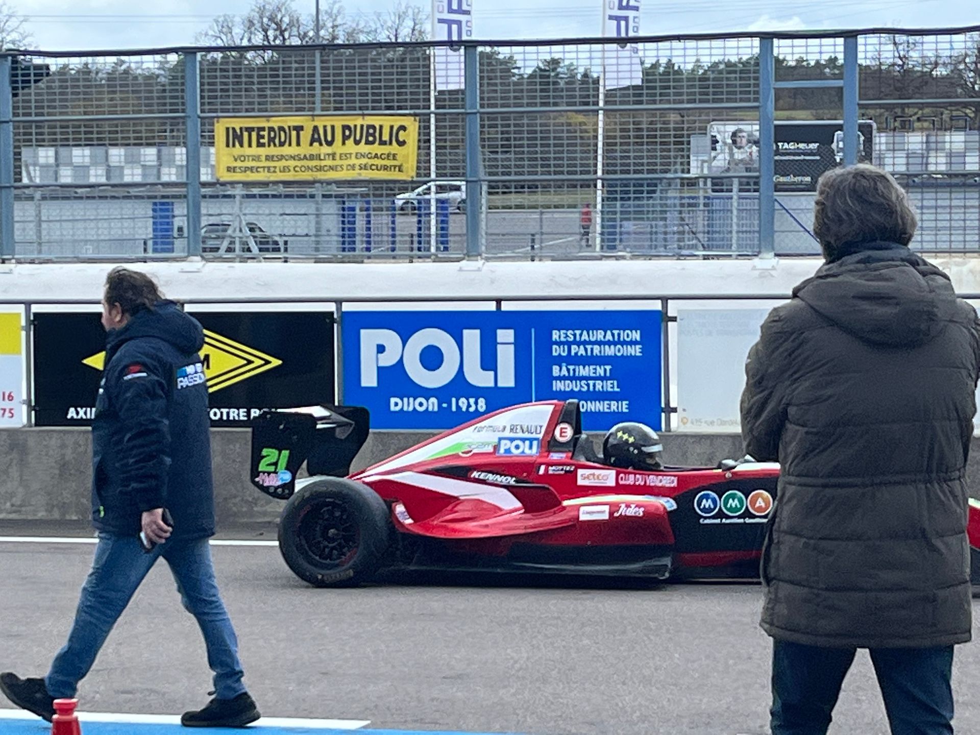 Voiture de course monoplace sur circuit, préparée pour la course, avec deux personnes habillées chaudement au premier plan