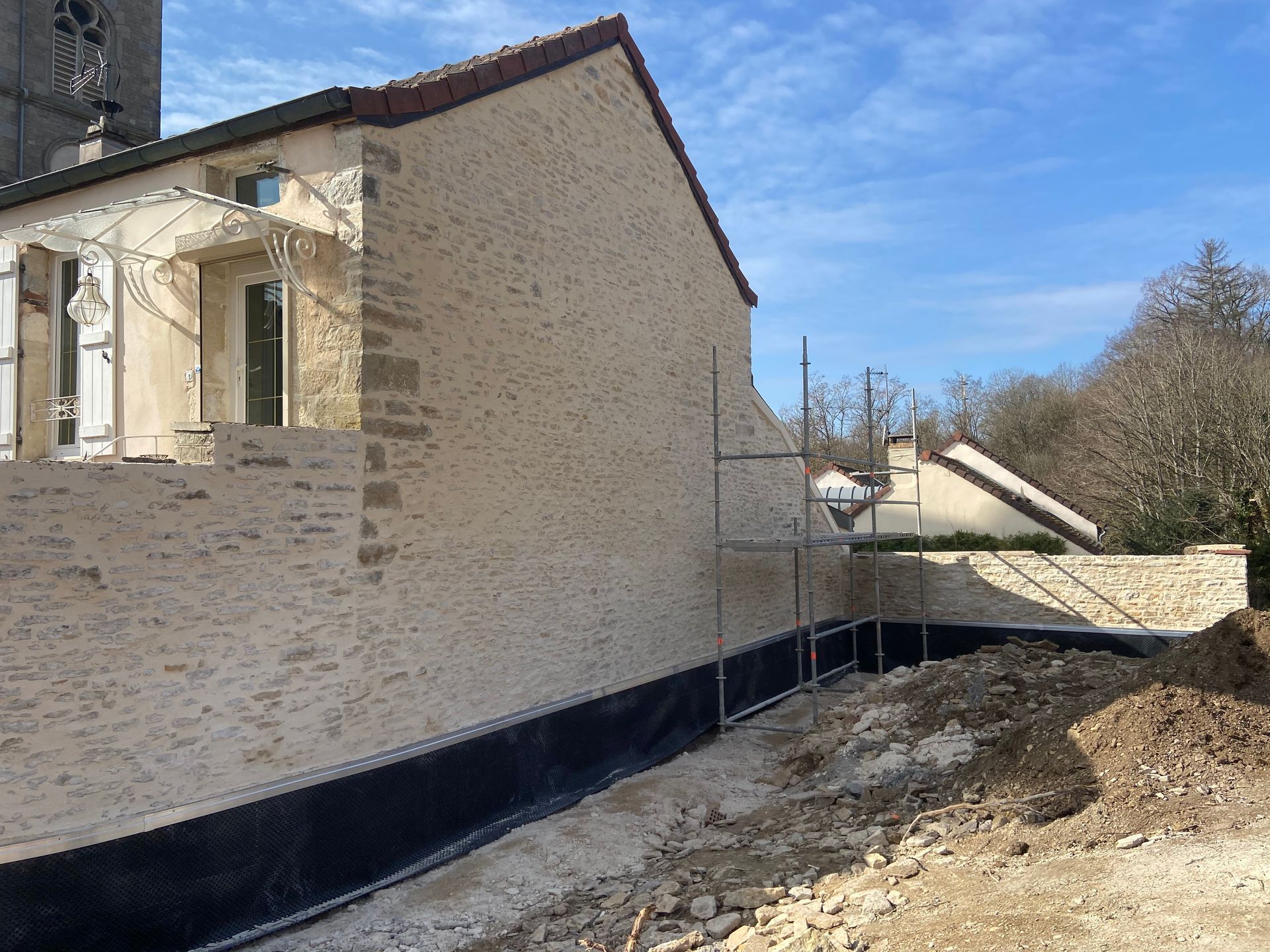 Bâtiment ancien en pierre avec des fenêtres et un mur en pierre apparente complètement refait.
