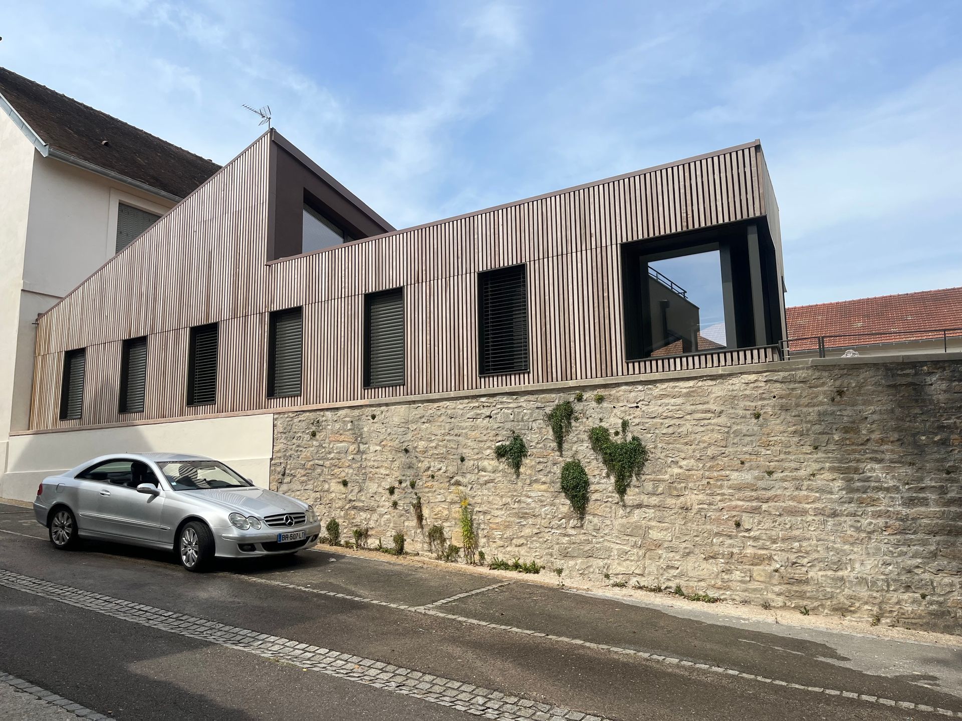 Maison moderne avec un mur en pierre et une voiture garée.
