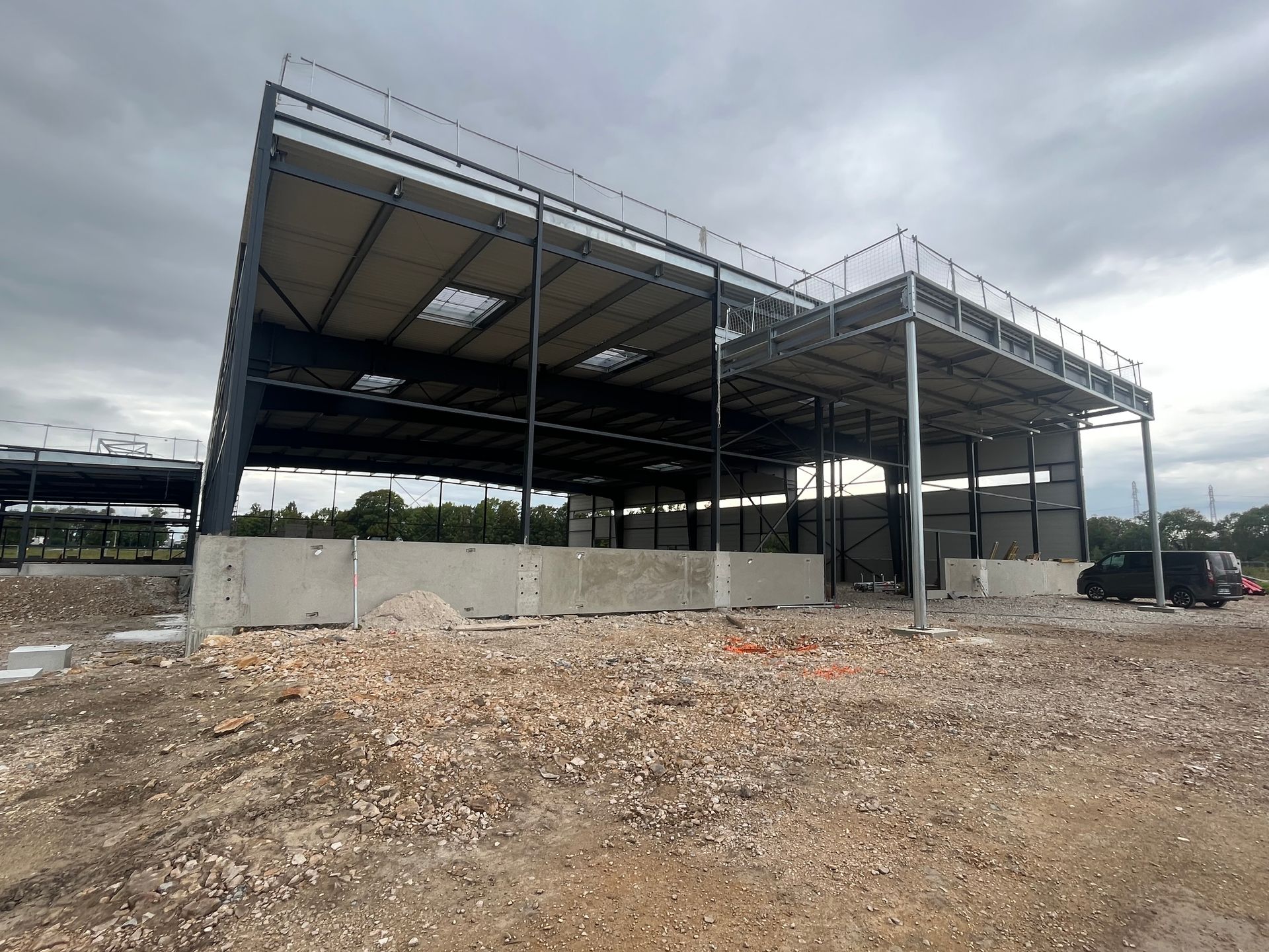 Bâtiment industriel moderne avec des structures en métal et un toit partiellement construit. Le ciel est clair et ensoleillé.
