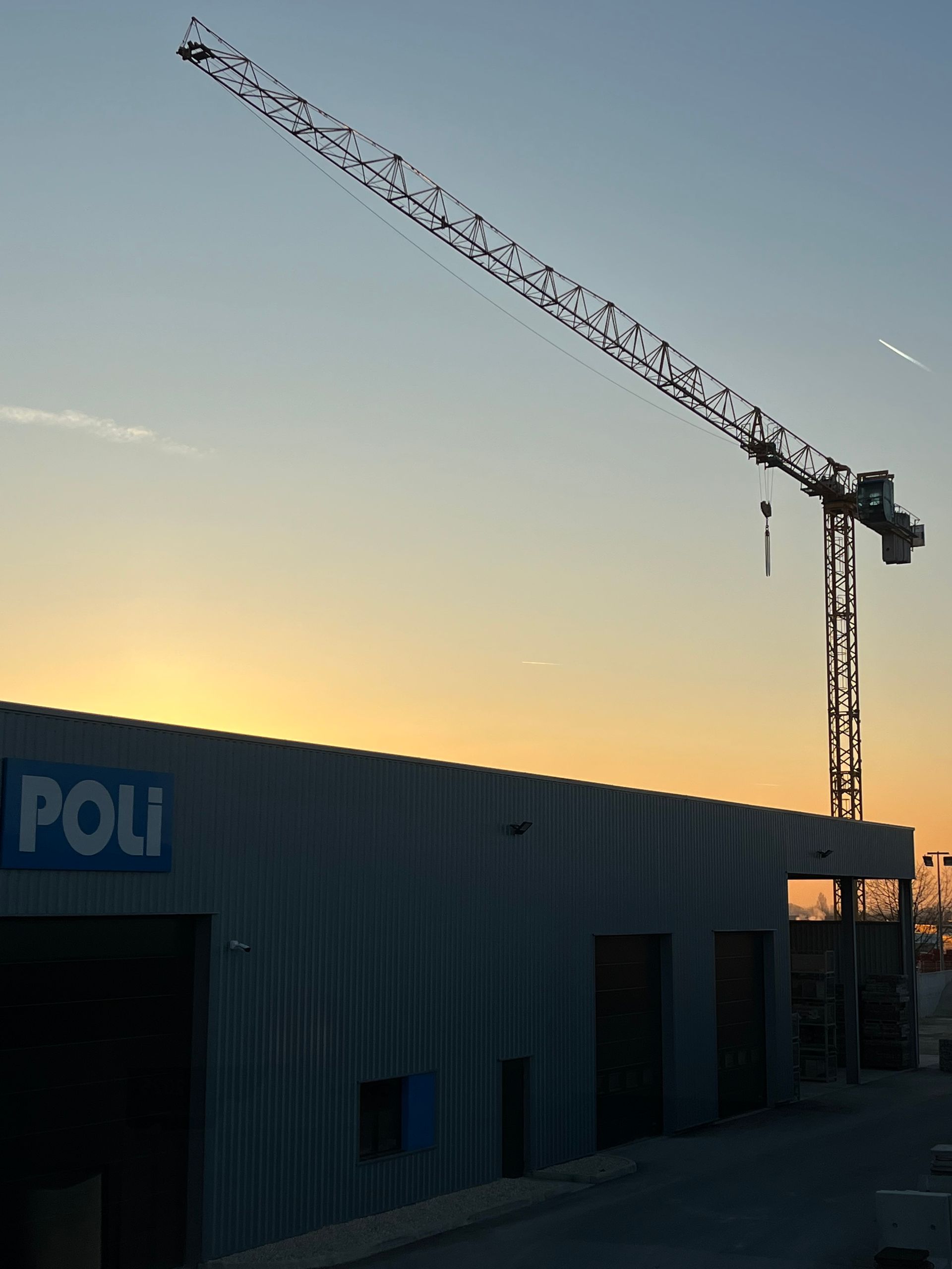 Grue de construction au coucher du soleil devant un bâtiment marqué 