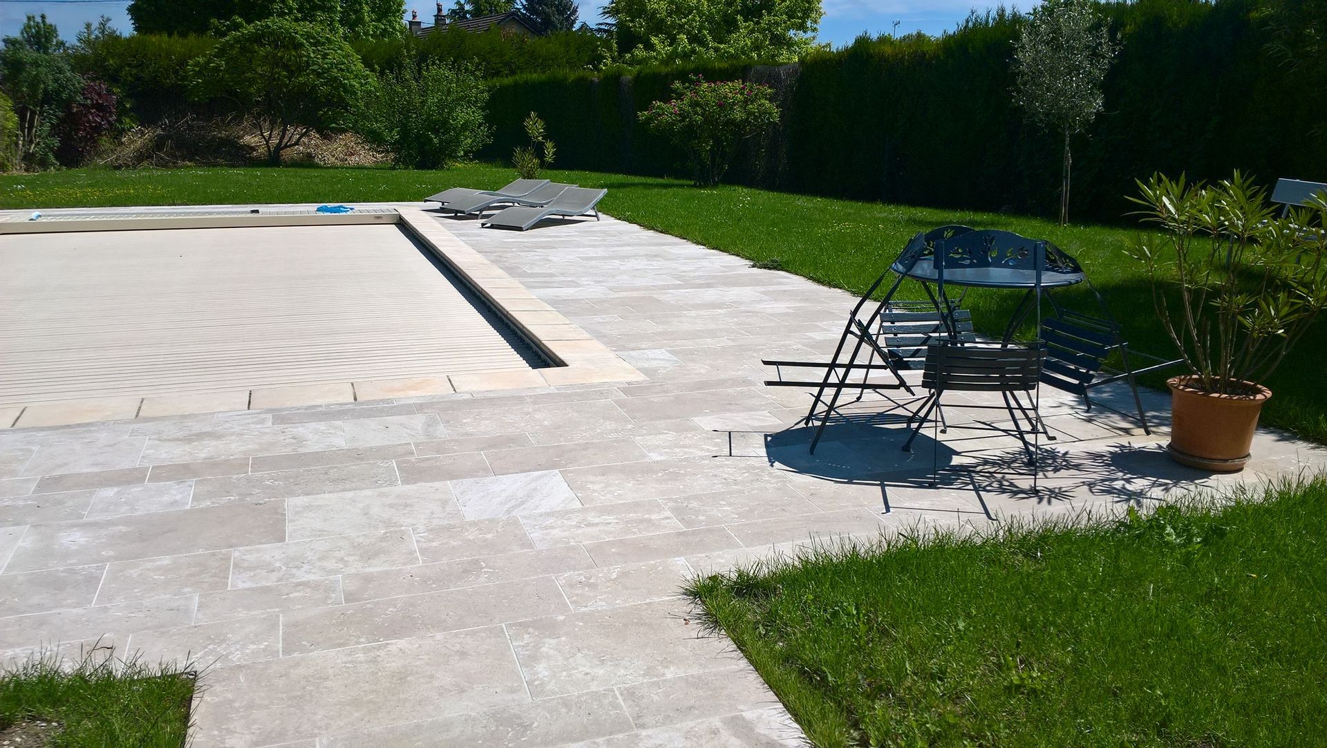 Jardin moderne avec terrasse en pierres et piscine couverte. Un espace extérieur bien aménagé avec des chaises et une table.