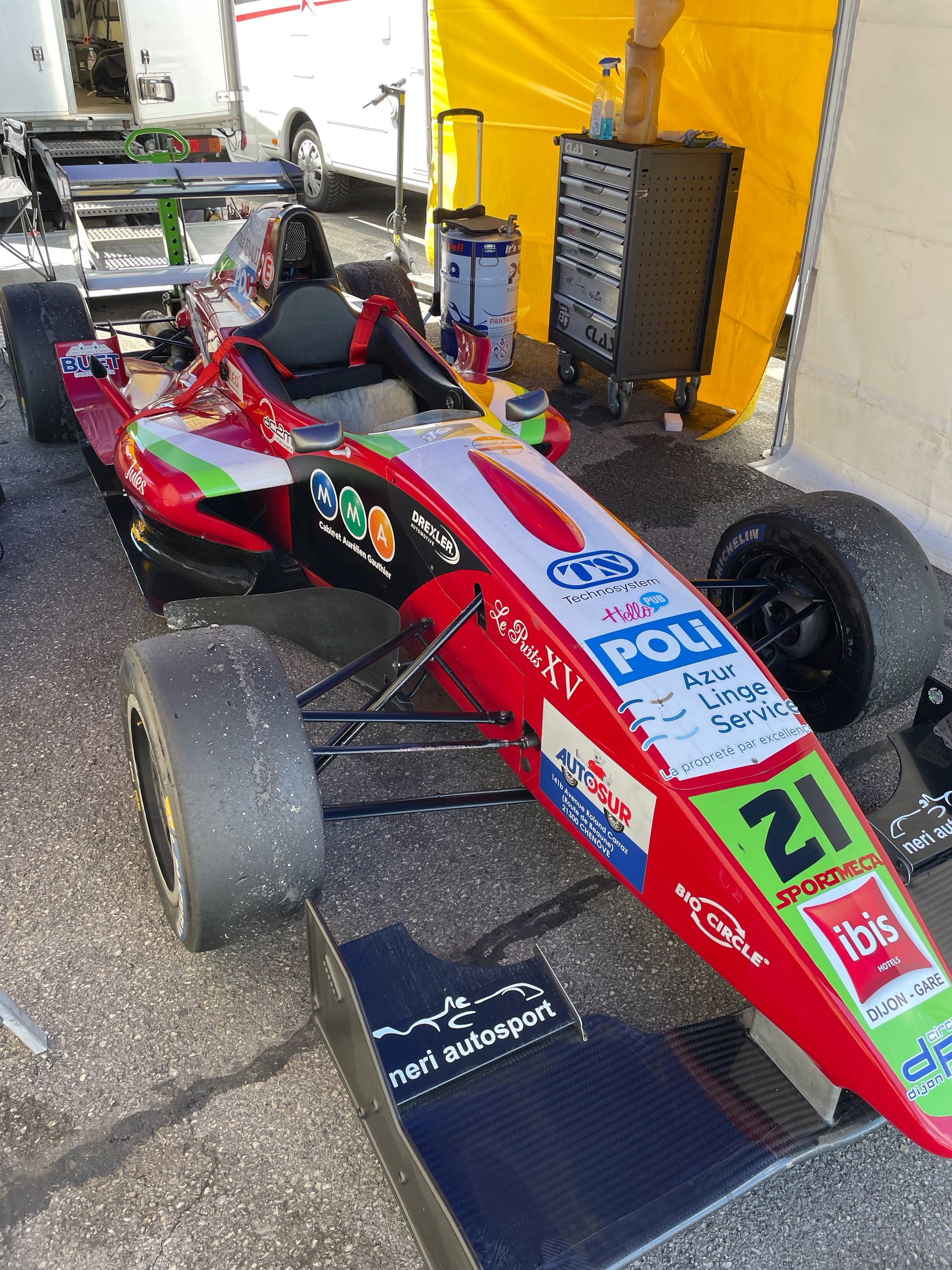 Monoplace rouge numéro 21 décorée d'autocollants sponsors, vue de dessus dans un paddock