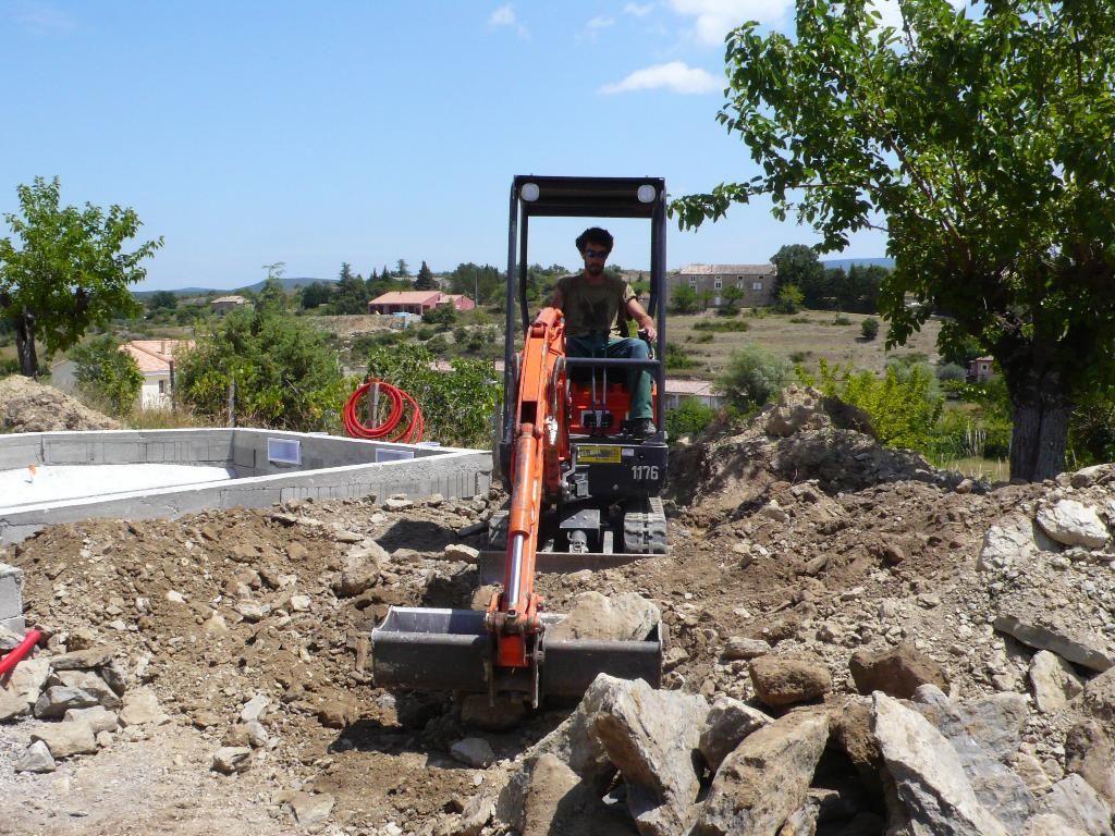 Un homme conduit une excavatrice sur un chantier, déplaçant de la terre et des pierres.