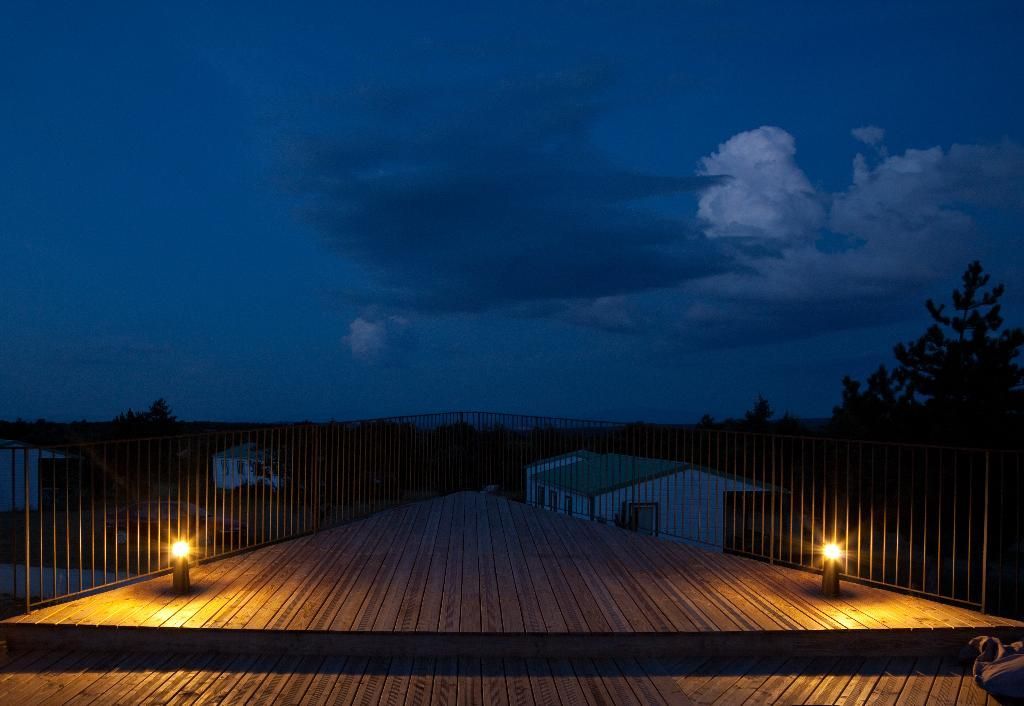 Passerelle en bois éclairée par des lampes la nuit, avec un ciel sombre.