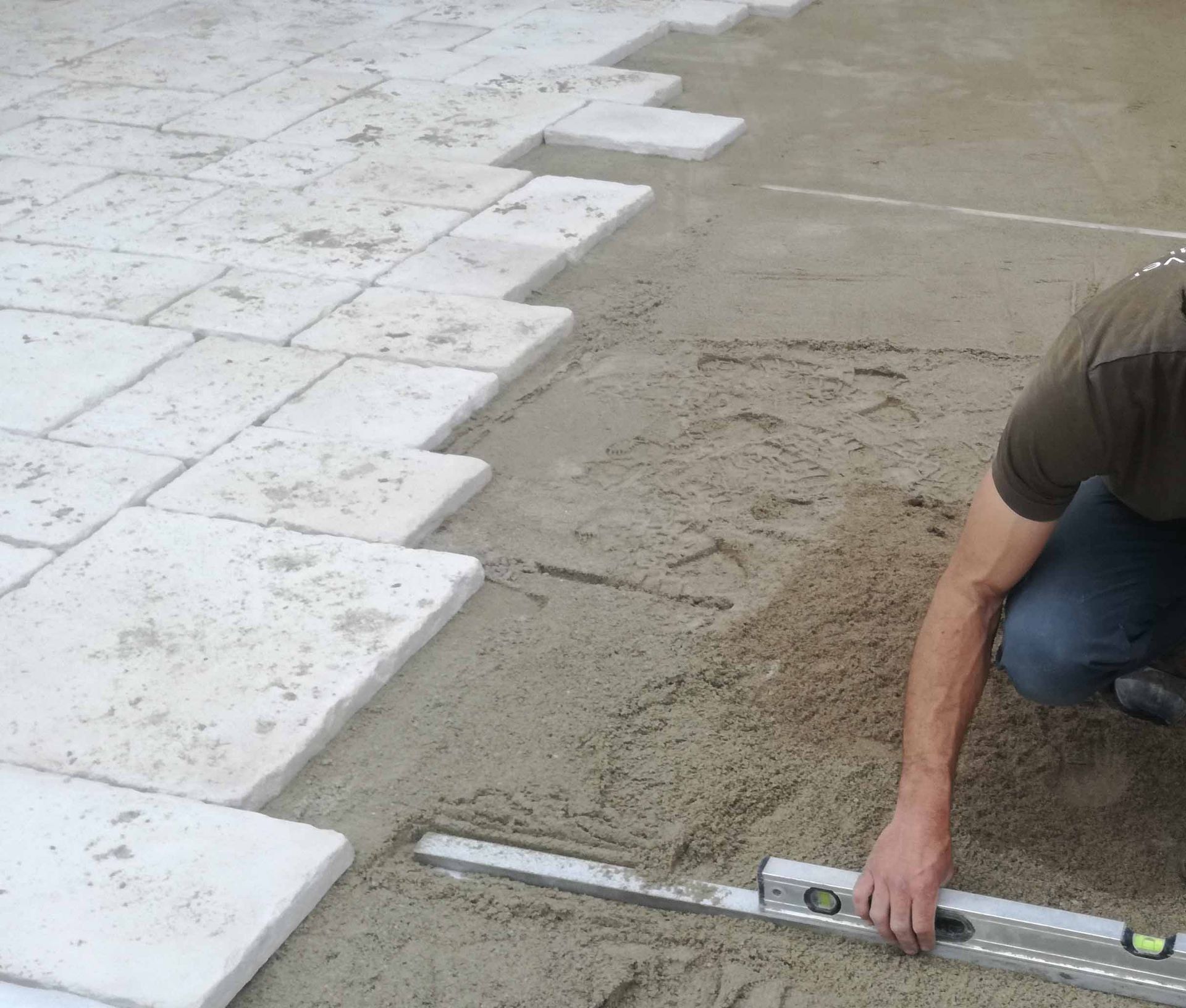 Personne nivelant des pierres de patio avec un niveau à bulle sur une base de sable.