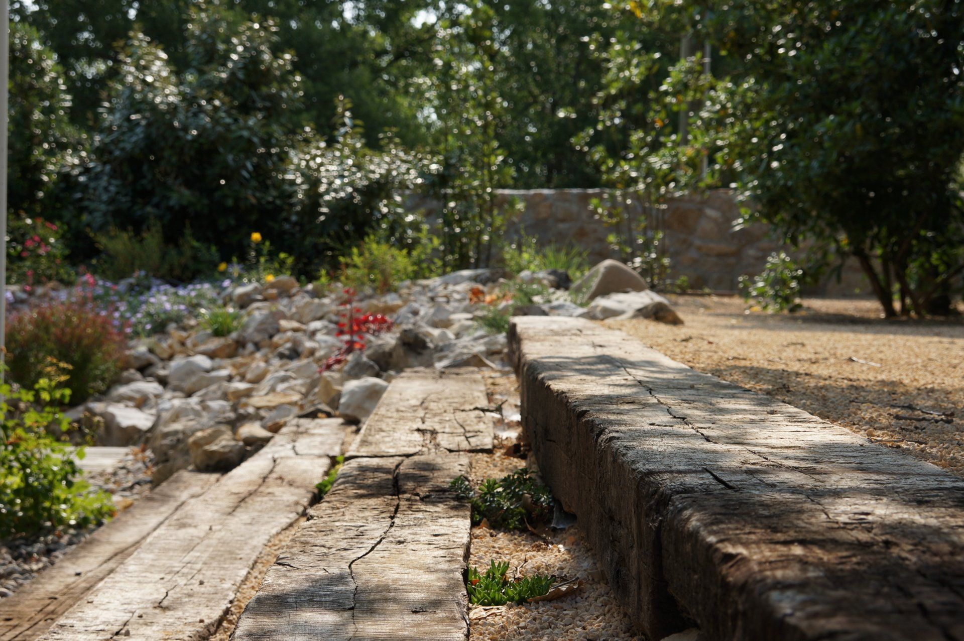 Création d'un chemin avec des marches en bois qui mènent à un jardin de rocaille avec des fleurs colorées et des arbres.