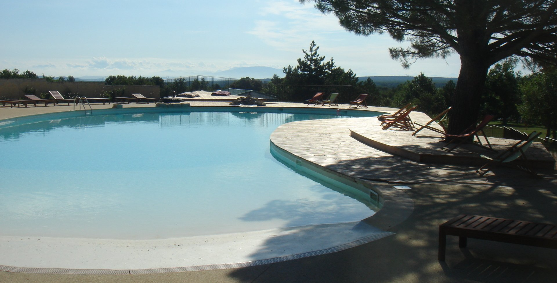 Conception d'une piscine attrayante avec des transats offrant une vue sur une lointaine chaîne montagneuse sous un ciel ensoleillé.