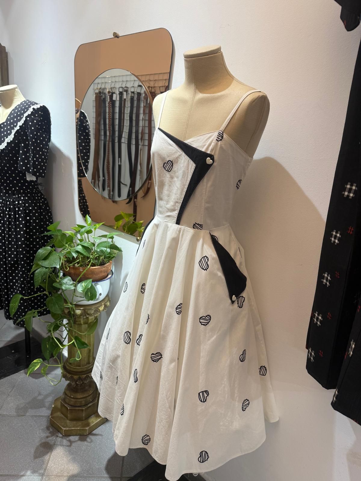 Interior de una tienda vintage con un espejo ornamentado, arte enmarcado y una exhibición de ropa y joyas.