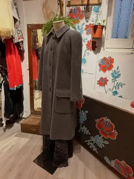Maniquí con un abrigo largo gris en una tienda con papel tapiz floral y un espejo.