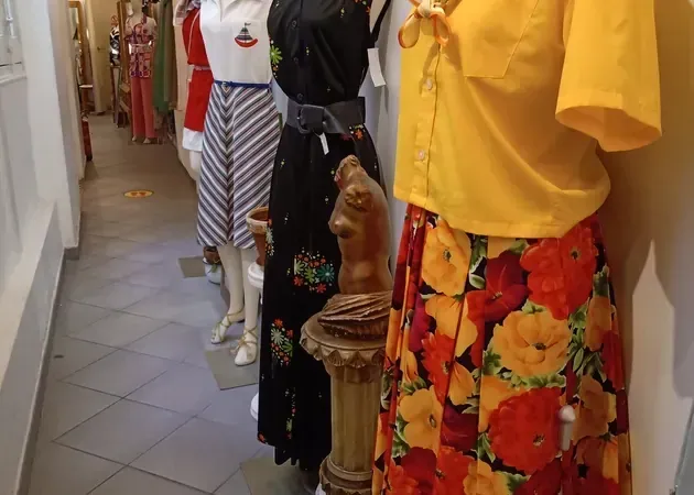 Los maniquíes exhiben ropa vintage en una tienda; se ven una falda floreada, un top amarillo y pantalones a rayas.