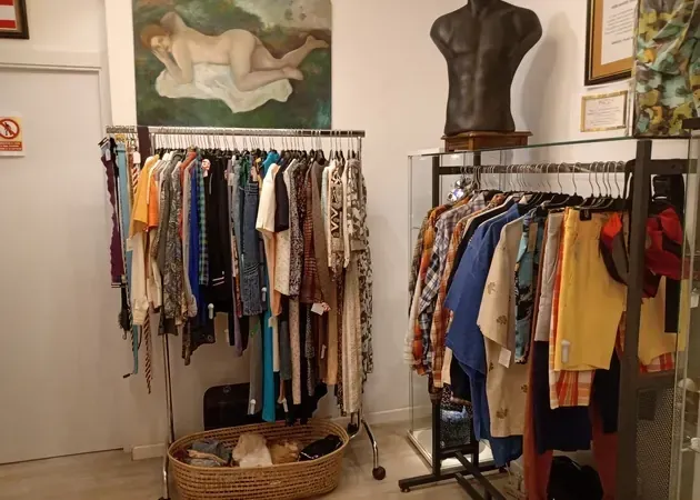 Percheros en una tienda de ropa vintage, con camisas, vestidos y un busto.