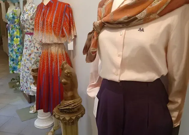 Exhibición de ropa con vestidos y una combinación de blusa y pantalón en una tienda. Colores: rojo, naranja, blanco y morado.