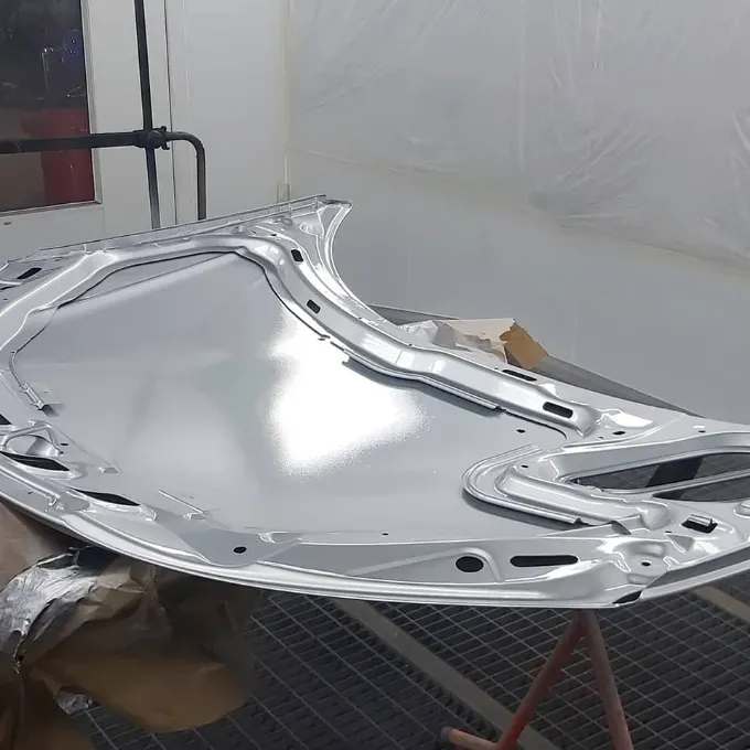 Capó de coche plateado recién pintado en cabina de pintura.