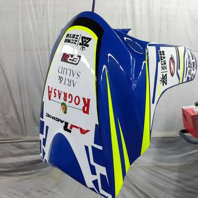 Carenado de motocicleta azul, blanco y amarillo con logotipos de patrocinadores, colgado en un taller.