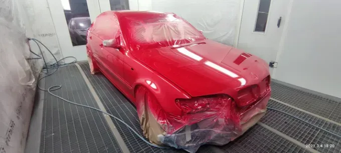 Coche rojo recién pintado en cabina de pintura.