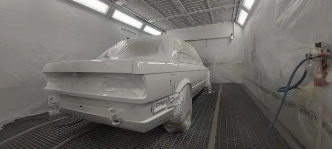 Un coche blanco dentro de una cabina de pintura. Está parcialmente cubierto con plástico protector.